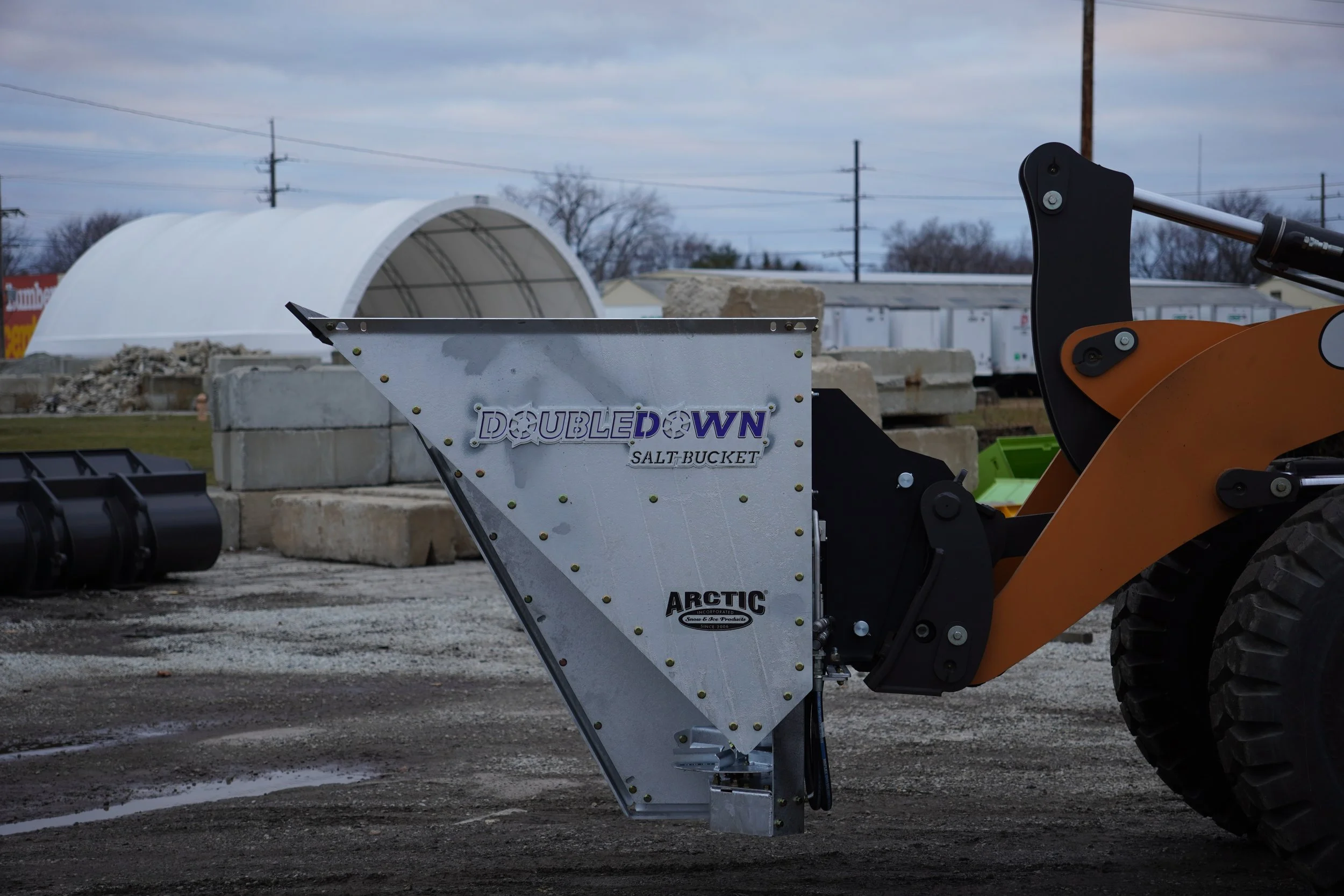 A beauty shot of a galvanized ARCTIC double down salt spreader mounted to a Case front end loader.