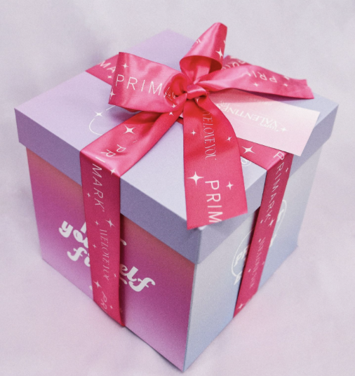 A pastel purple gift box with a pink satin ribbon tied in a bow on top, featuring white text and star patterns.