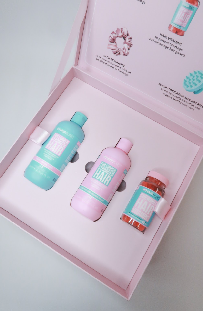 Pink box containing three bottles of hair care products, including shampoo and supplements, with labels featuring pink and turquoise colors.
