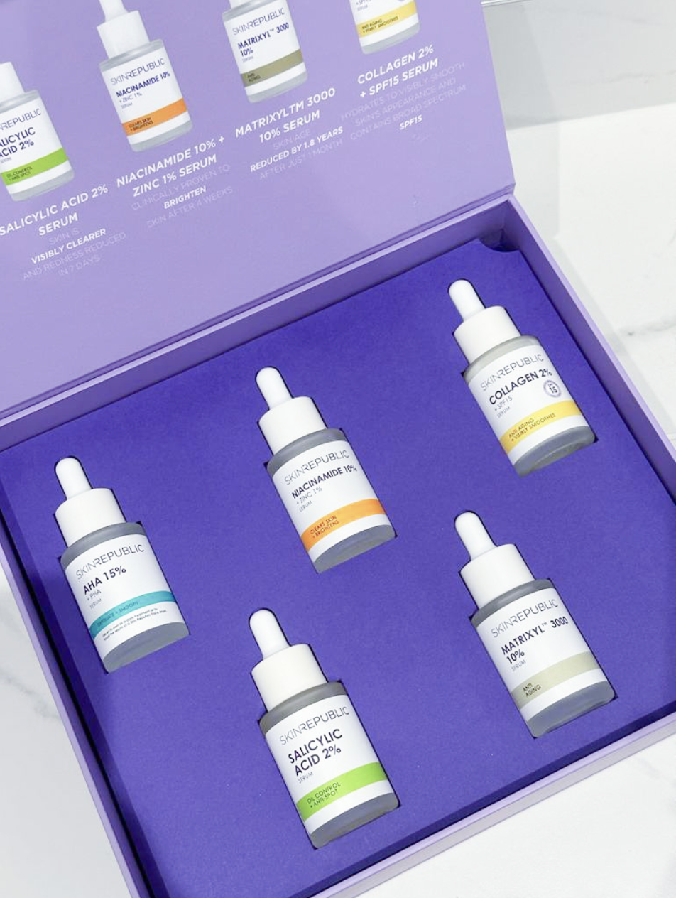 Set of five skincare serum bottles with dropper caps inside a purple box. Labels include ingredients like salicylic acid, niacinamide, AHA, matrixyl, collagen, and their respective percentages.