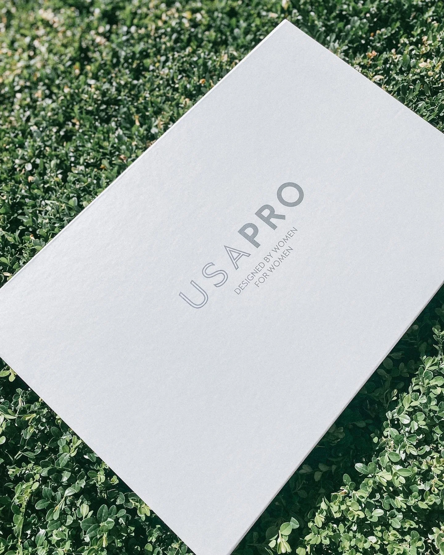 White cosmetics box labeled 'U CASA PRO' with subtitle 'Designed by Women for Women', resting on green foliage background.
