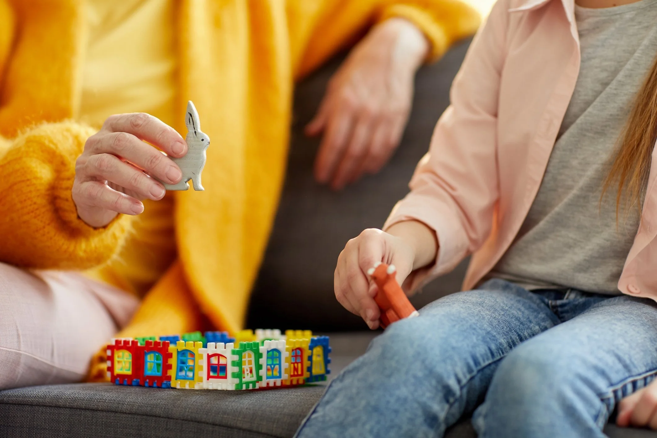 Close-up of a child's hand holding a small bunny toy, with playing blocks on a bench and an adult's hand in the background.