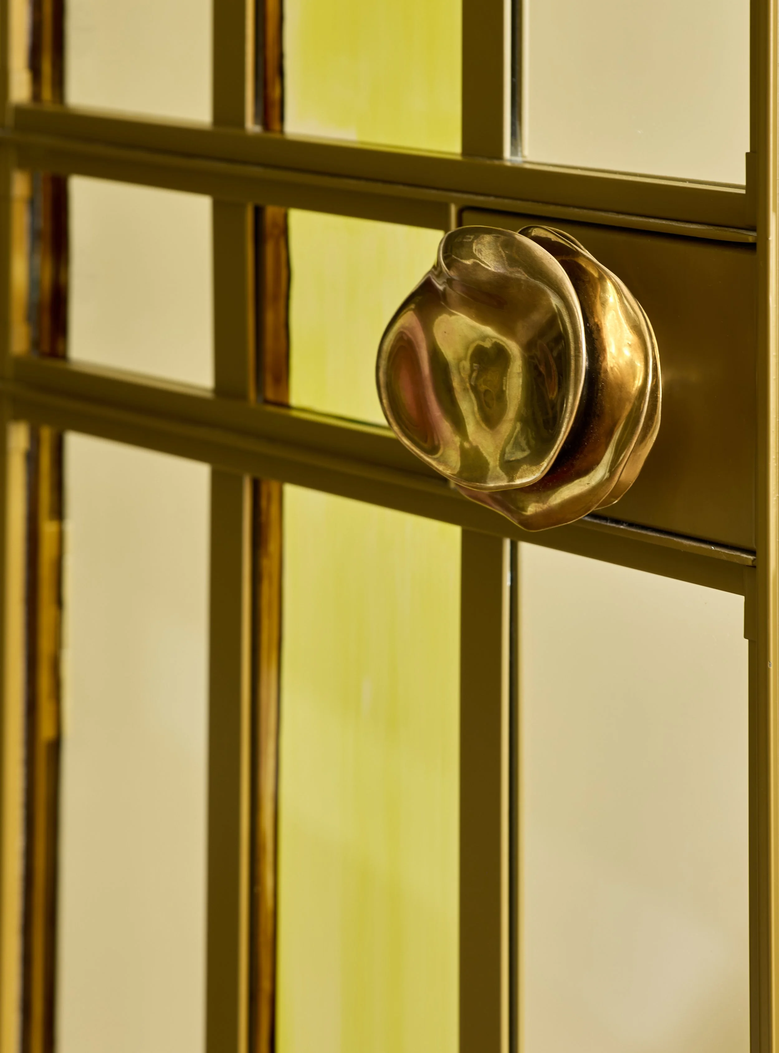 Close-up of a gold door handle on a metallic door with glass panels, with a blurred background.