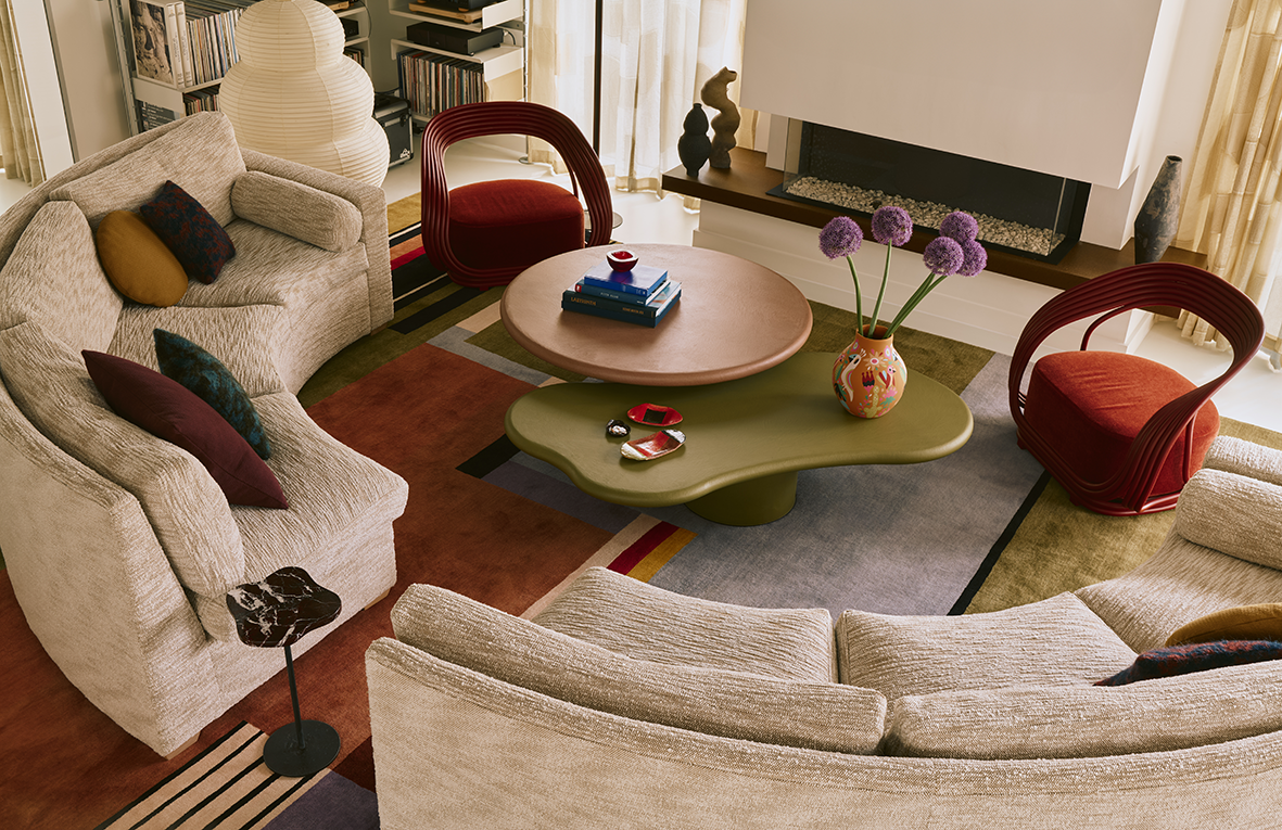 Living room with beige sofa, two red armchairs, a green coffee table with purple flowers in a vase, and a round wooden table with books and a small bowl.