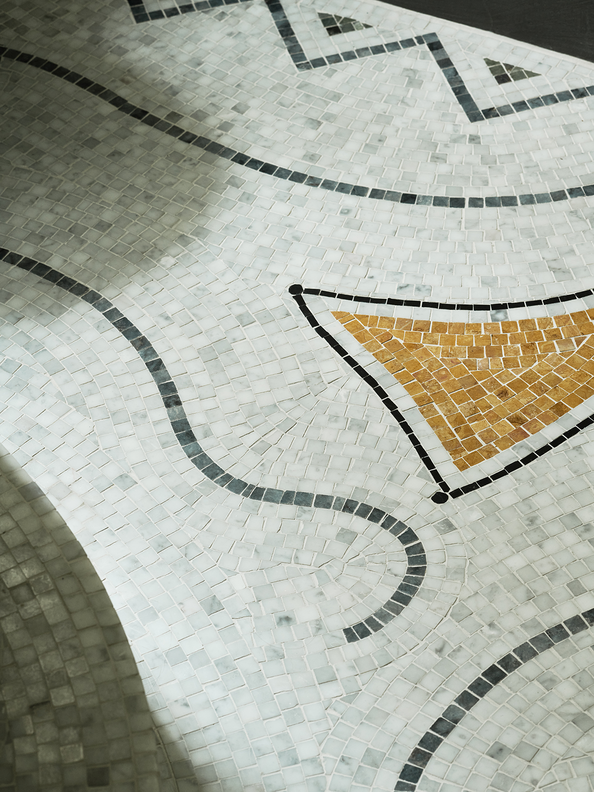 Close-up of a mosaic floor featuring a clock with black lines, a gold triangle, and gray background tiles.