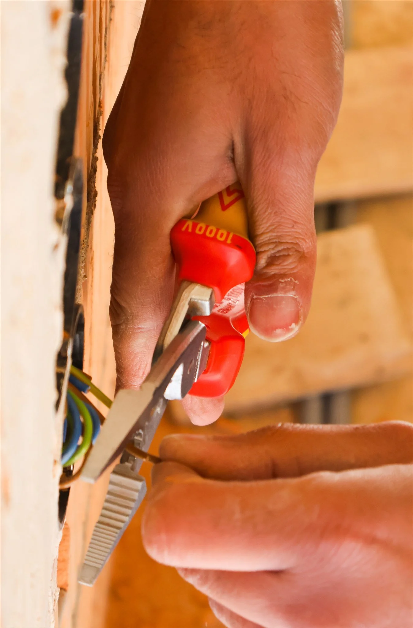 A person's hand working on an electrical panel with wiring, using pliers with a red handle.