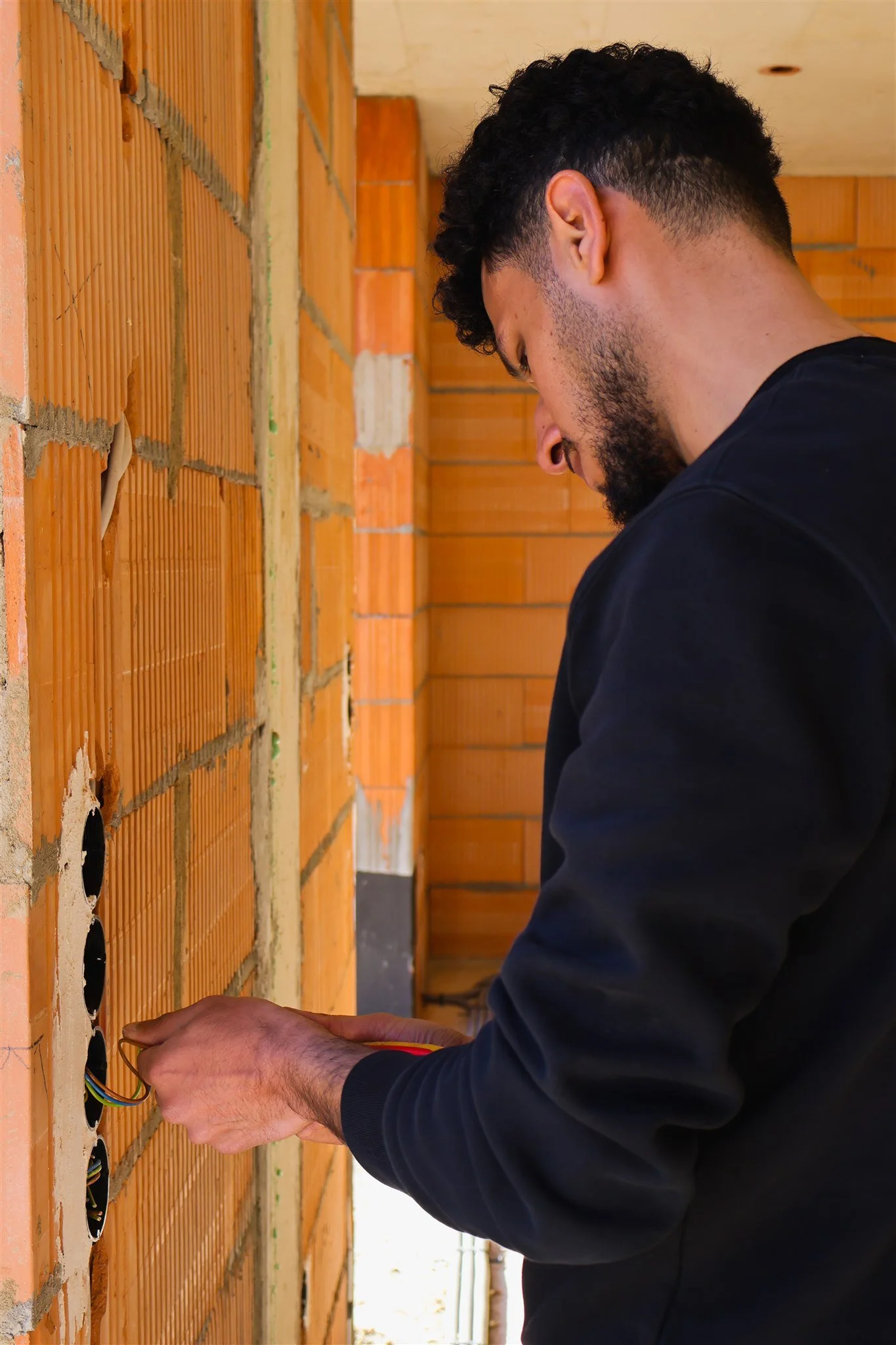A man working on electrical wiring in a brick wall under construction.
