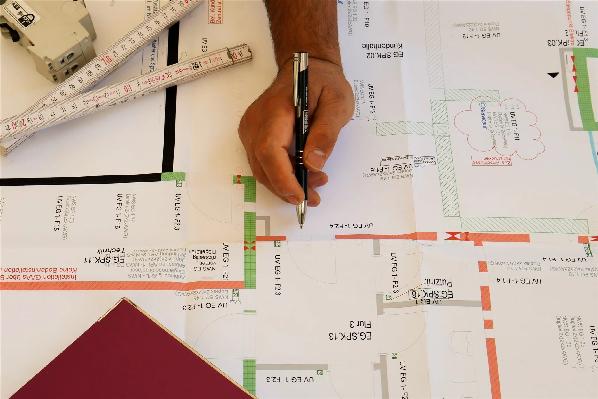 A person's hand with a black pen writing on a technical architectural blueprint, with rulers and other drafting tools on the paper.