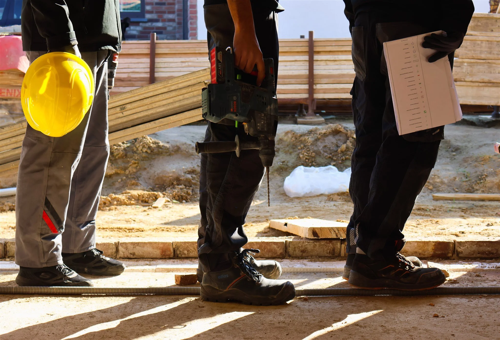 Construction workers standing on a building site, holding tools and a hard hat.