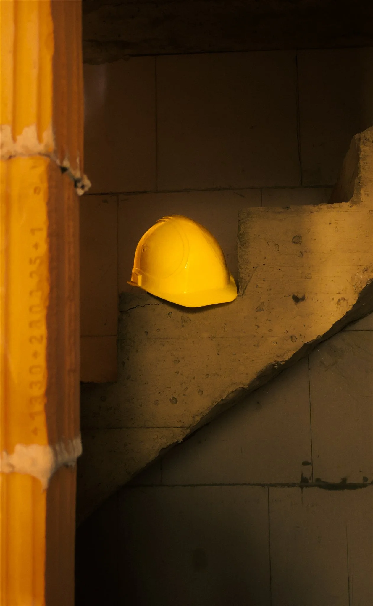 Yellow construction helmet resting against a stone and tile staircase, with a wooden measuring stick on the left side of the image.
