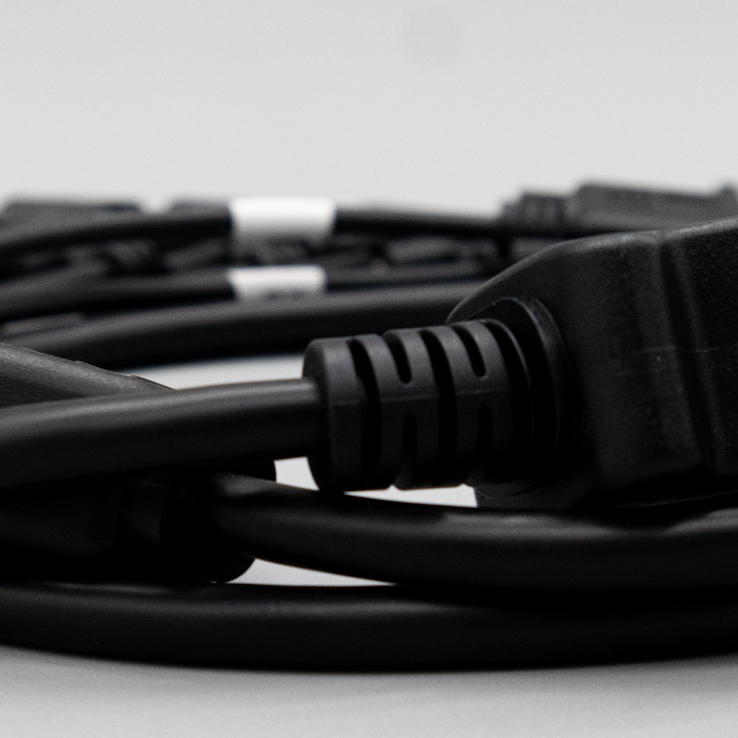 Close-up of multiple black electrical cords and a three-prong power plug on a white background.