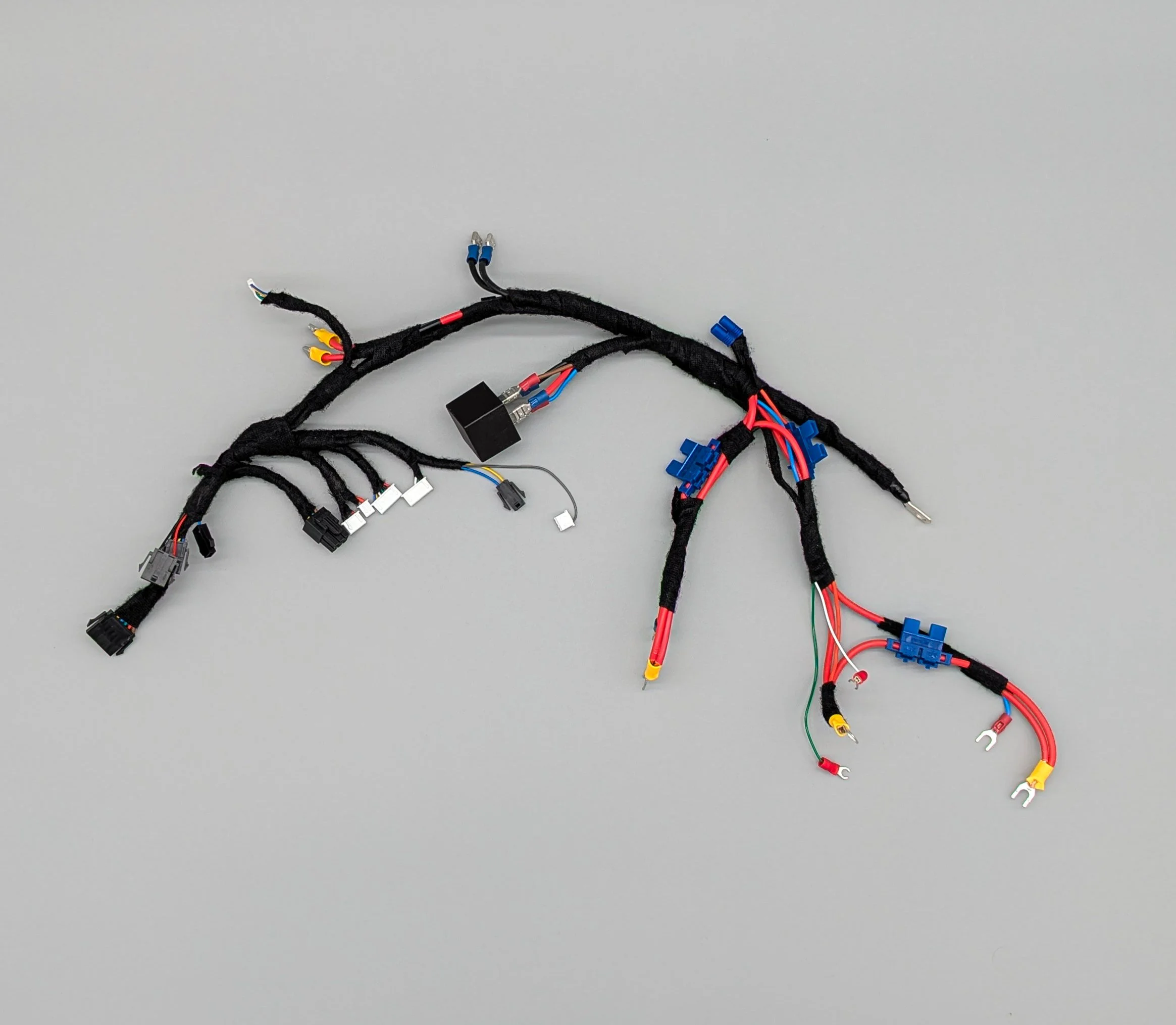 Automotive wiring harness with various colored wires, connectors, and protective sheathing on a gray surface.