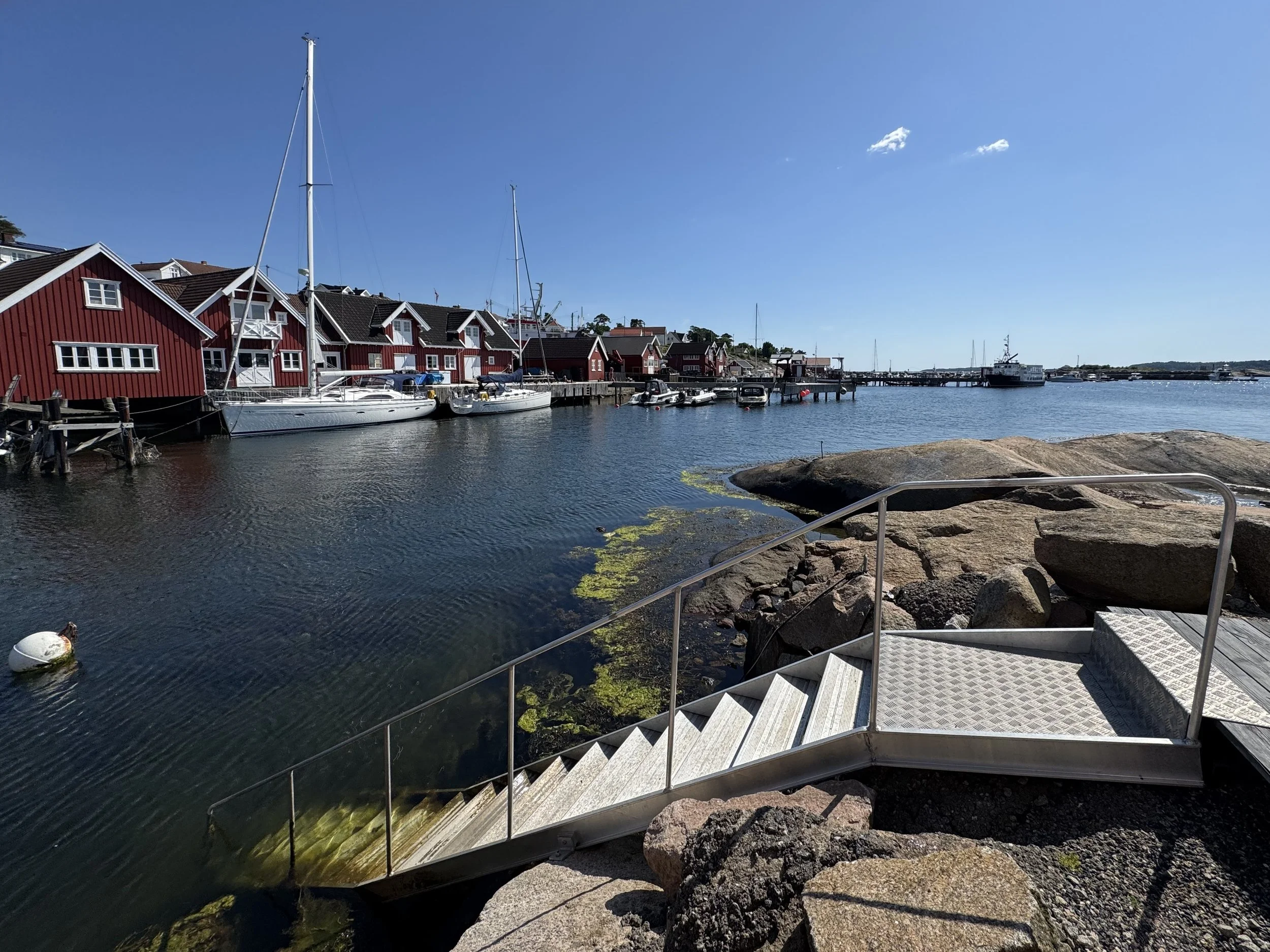 Sunt havn med fem seilbåter og røde trehus langs vannet, med en metalltrapp som fører ned til vannet og store steiner på østsiden.