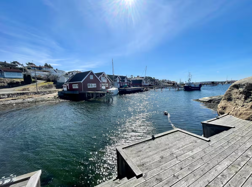 Sjøpromenade med små trehus, båter og en klar blå himmel.