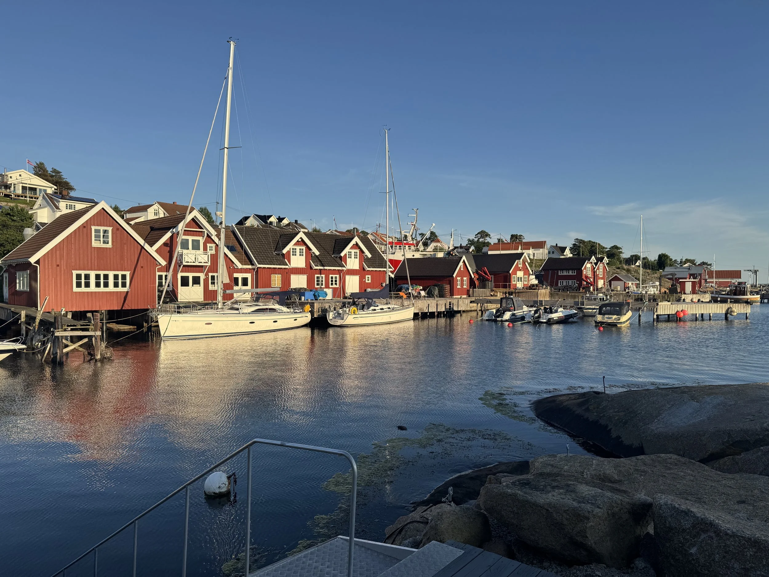 Søplace med røde trebygninger, båter i vannet og en klar blå himmel.