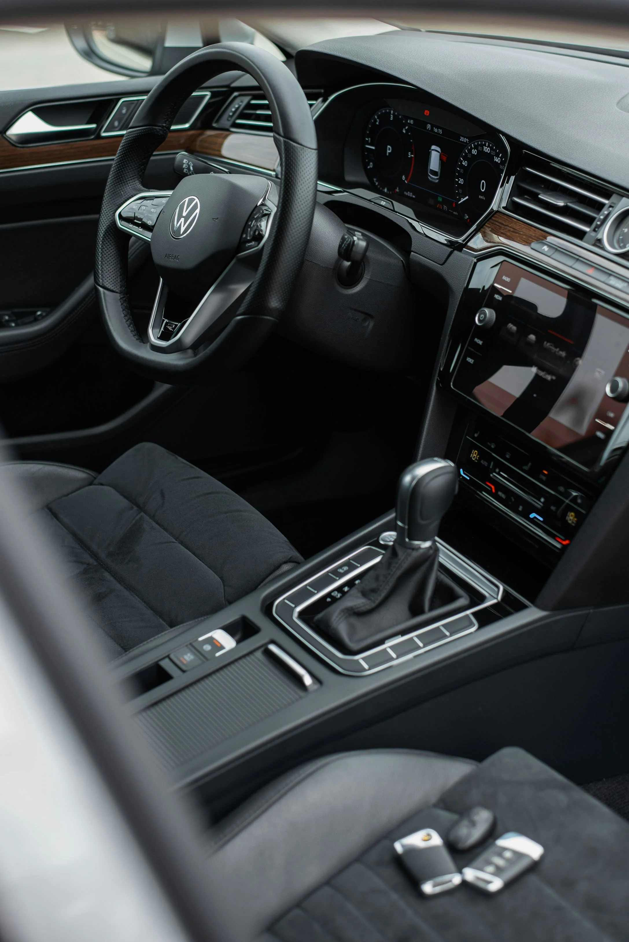 Interior of a modern Volkswagen car showing the steering wheel, digital dashboard, center console with a gear shifter, and key fob on the seat.