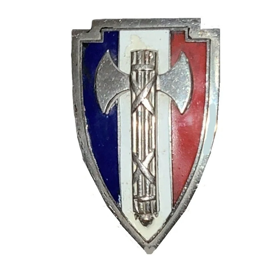 A shield-shaped badge featuring a silver axe crossed with a silver sword, with a background of the French flag's blue, white, and red vertical stripes.