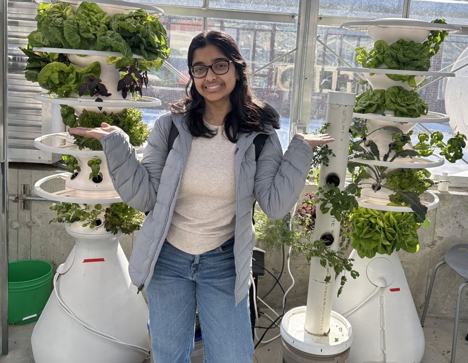 Student in greenhouse with vegetables in the background.