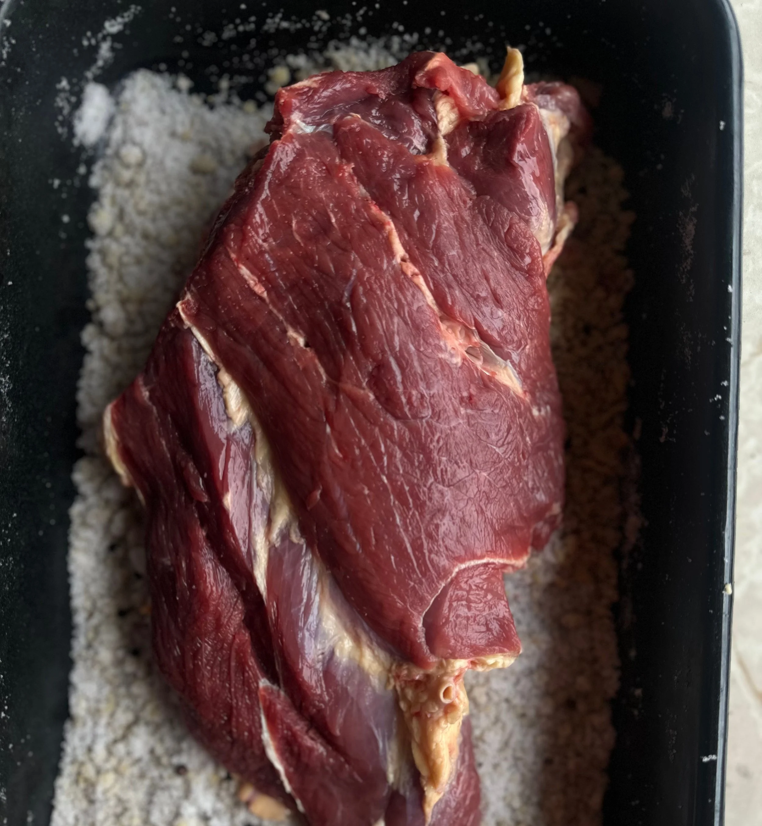 Sirovi komad crvenog mesa, govedina, postavljen na podlogu sa začinima u crnoj posudi.
