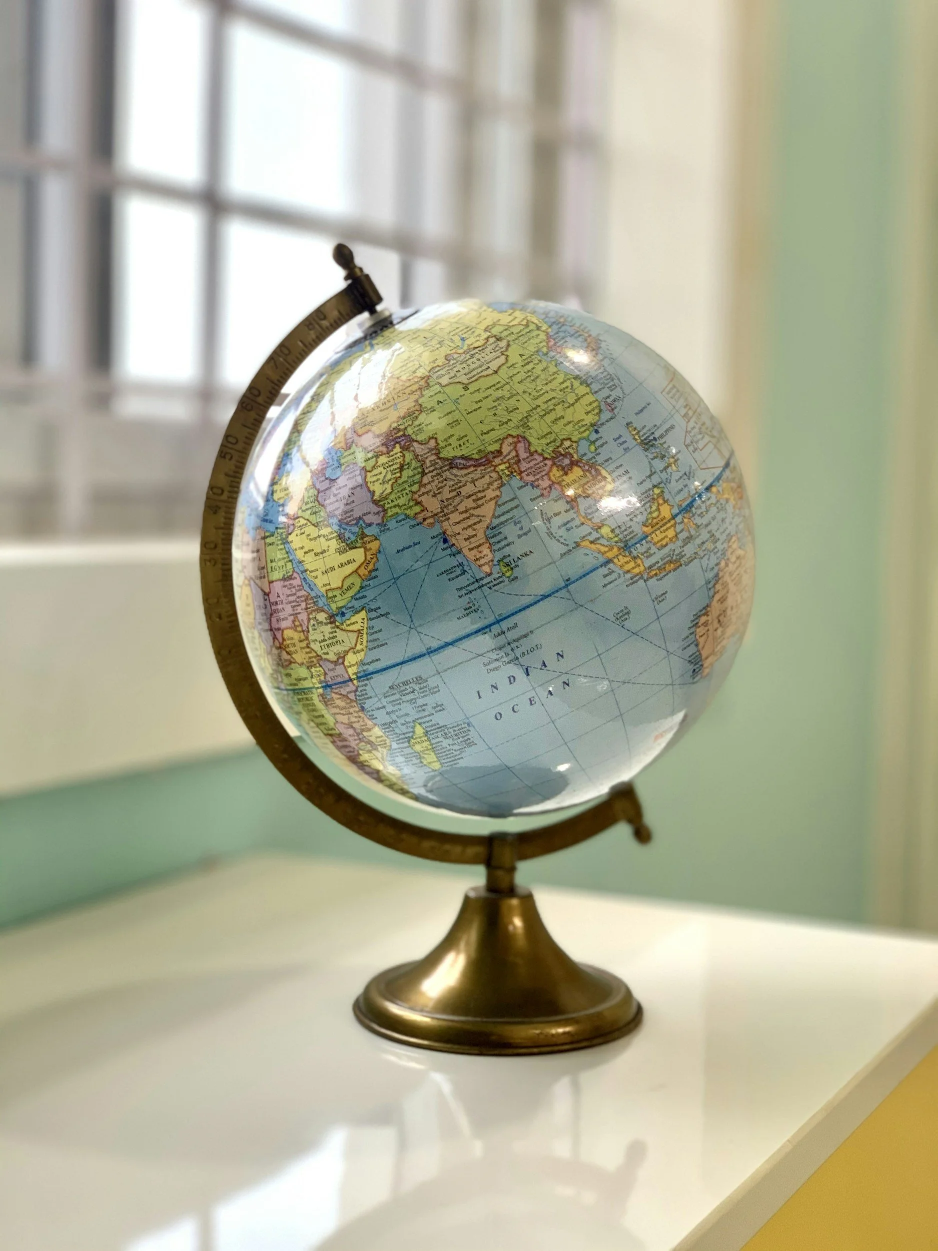 A globe showing Asia, the Middle East, and parts of Africa and Europe, placed on a white surface with a window in the background.