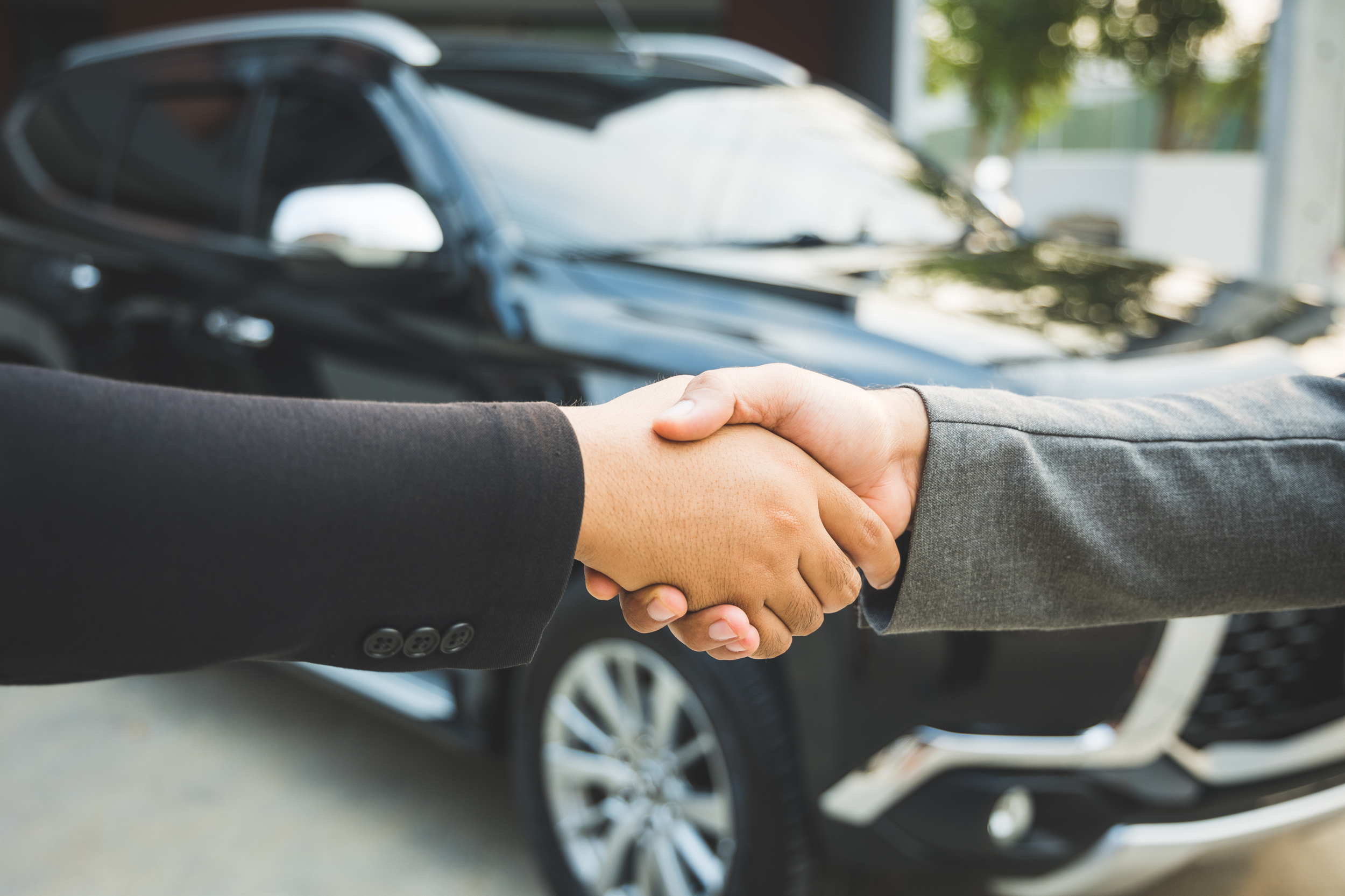 Two people making a deal in front of a car