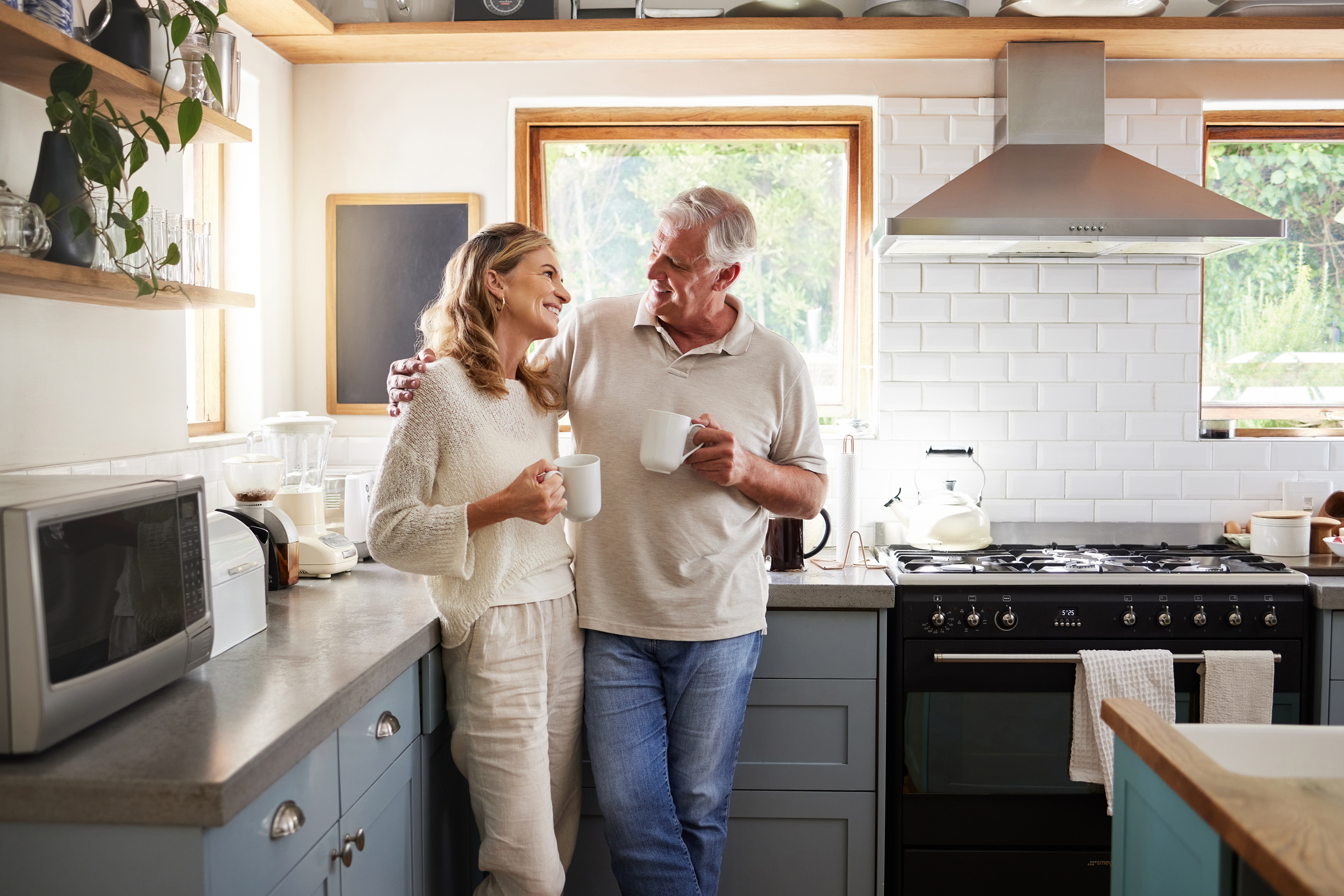 Happy smile and hug of a elderly woman and man with tea in a house kitchen together with quality time