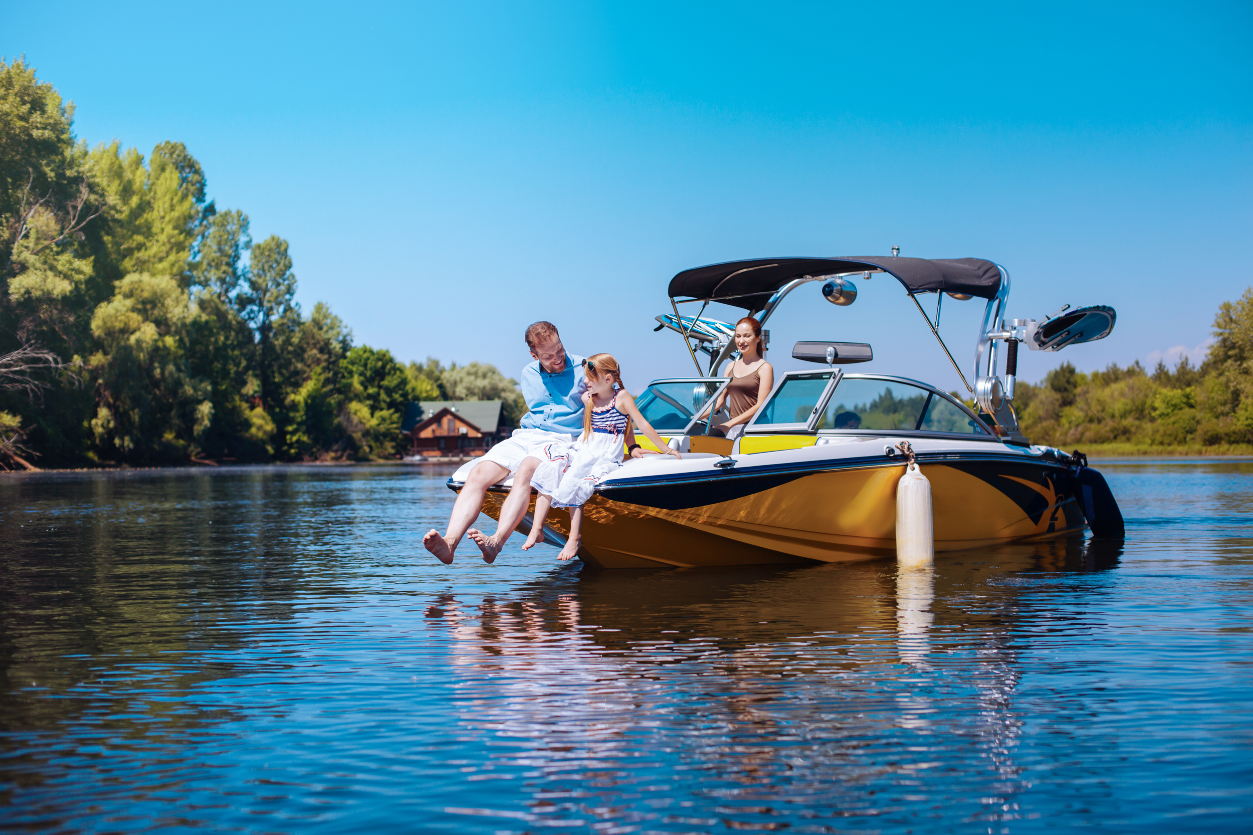 Caring young father and his little daughter sitting on the bow of the boat together while the mother observing them fondly 