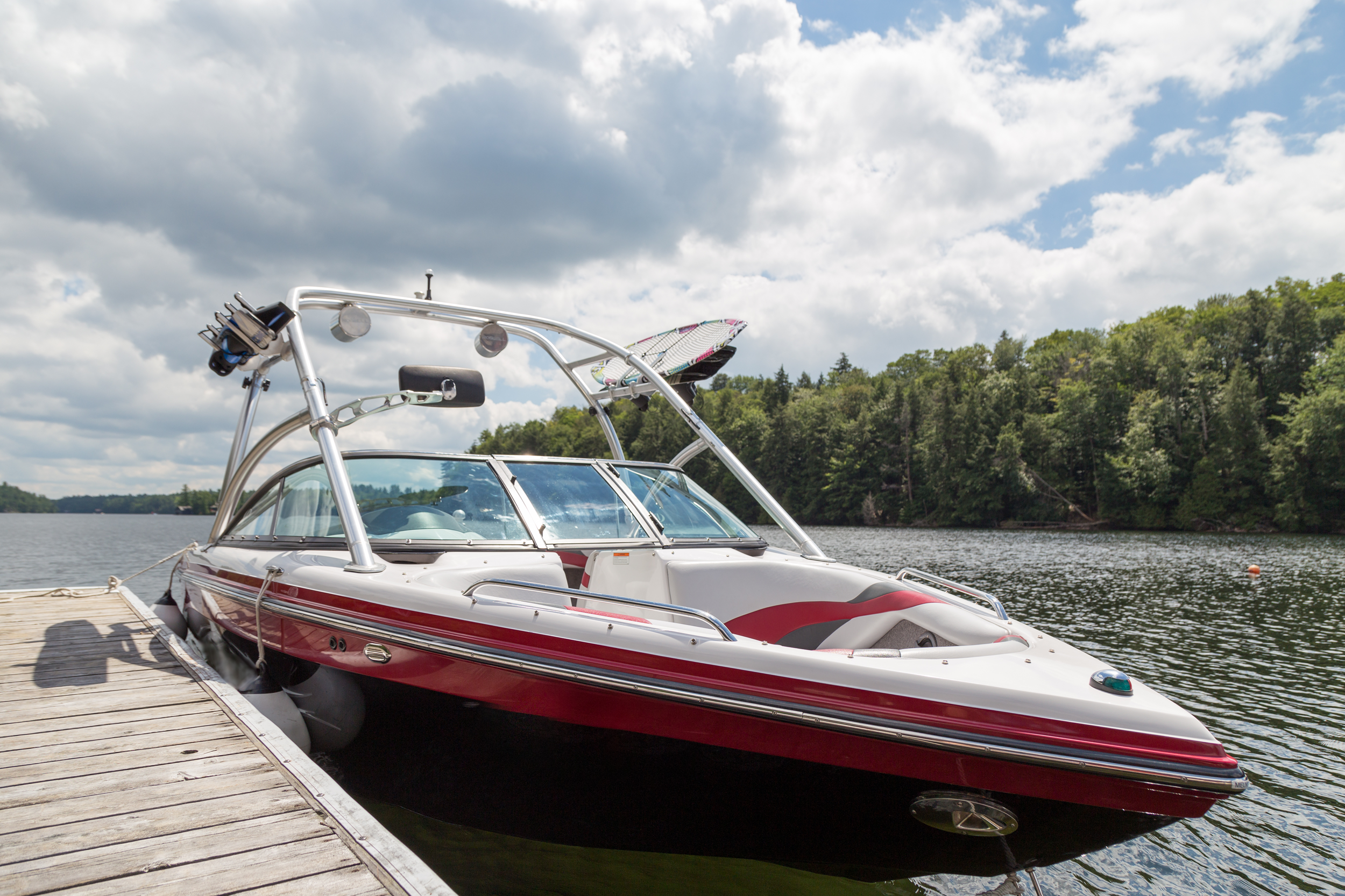 A wakeboard boat at a wooden dock in the Muskokas on a sunny day