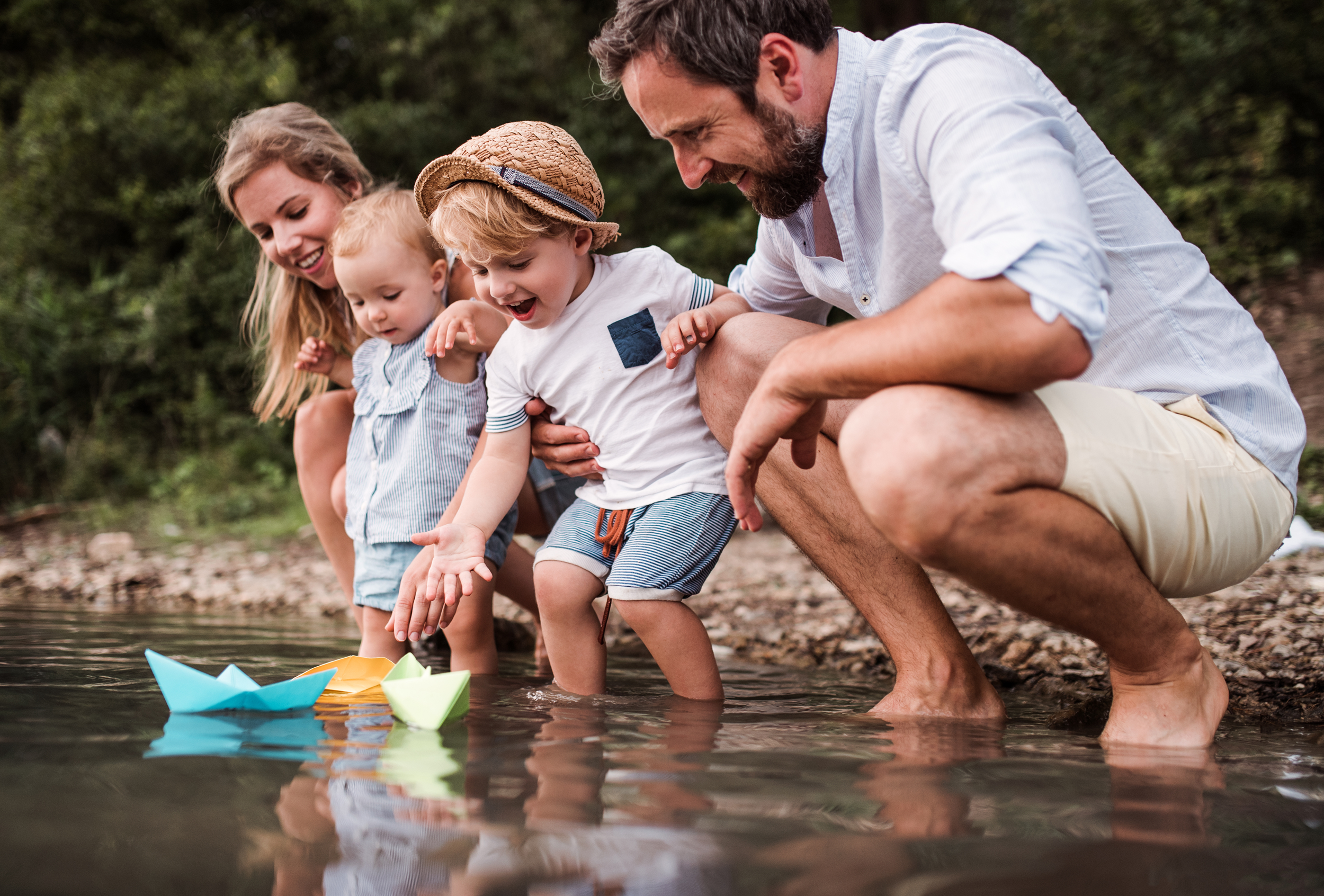 Young family with two toddler children outdoors by the river in summer, playing