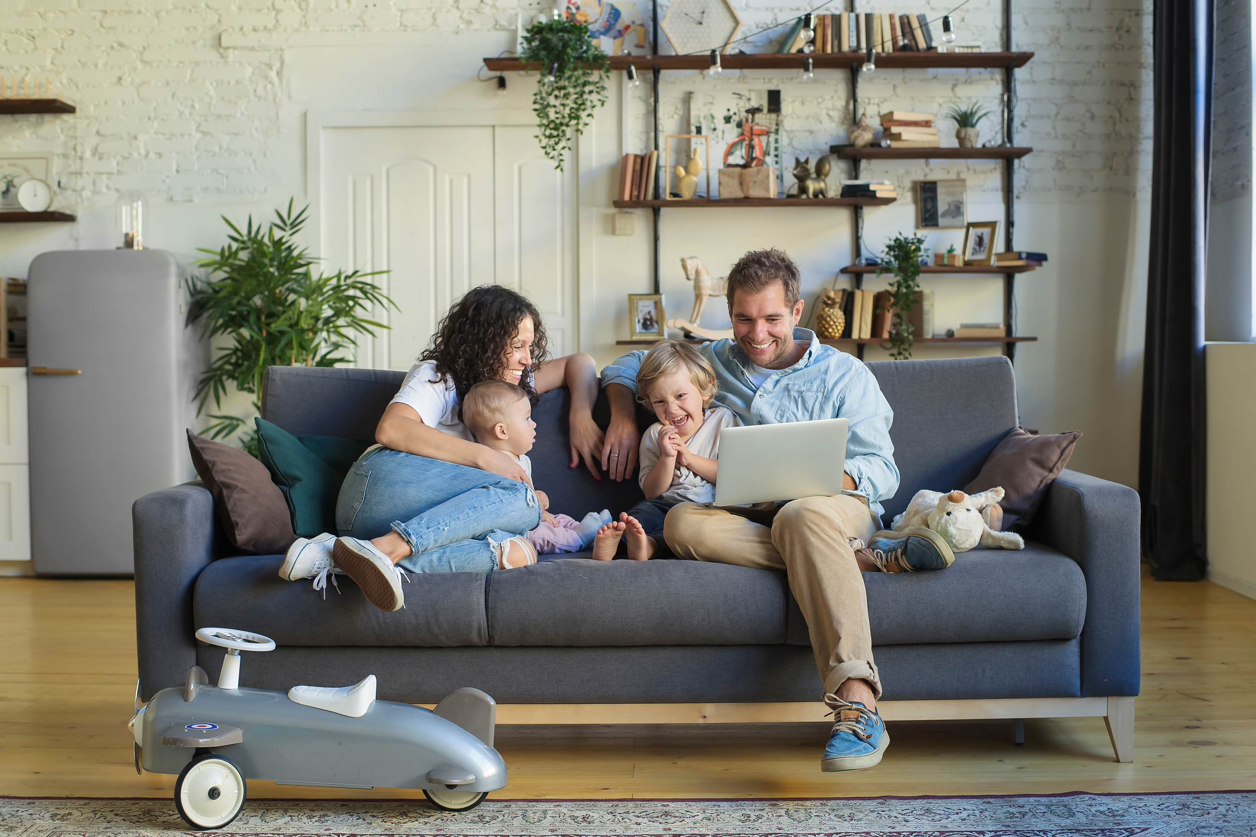 Mom and dad sitting on the couch with their two young kids looking at the laptop smiling