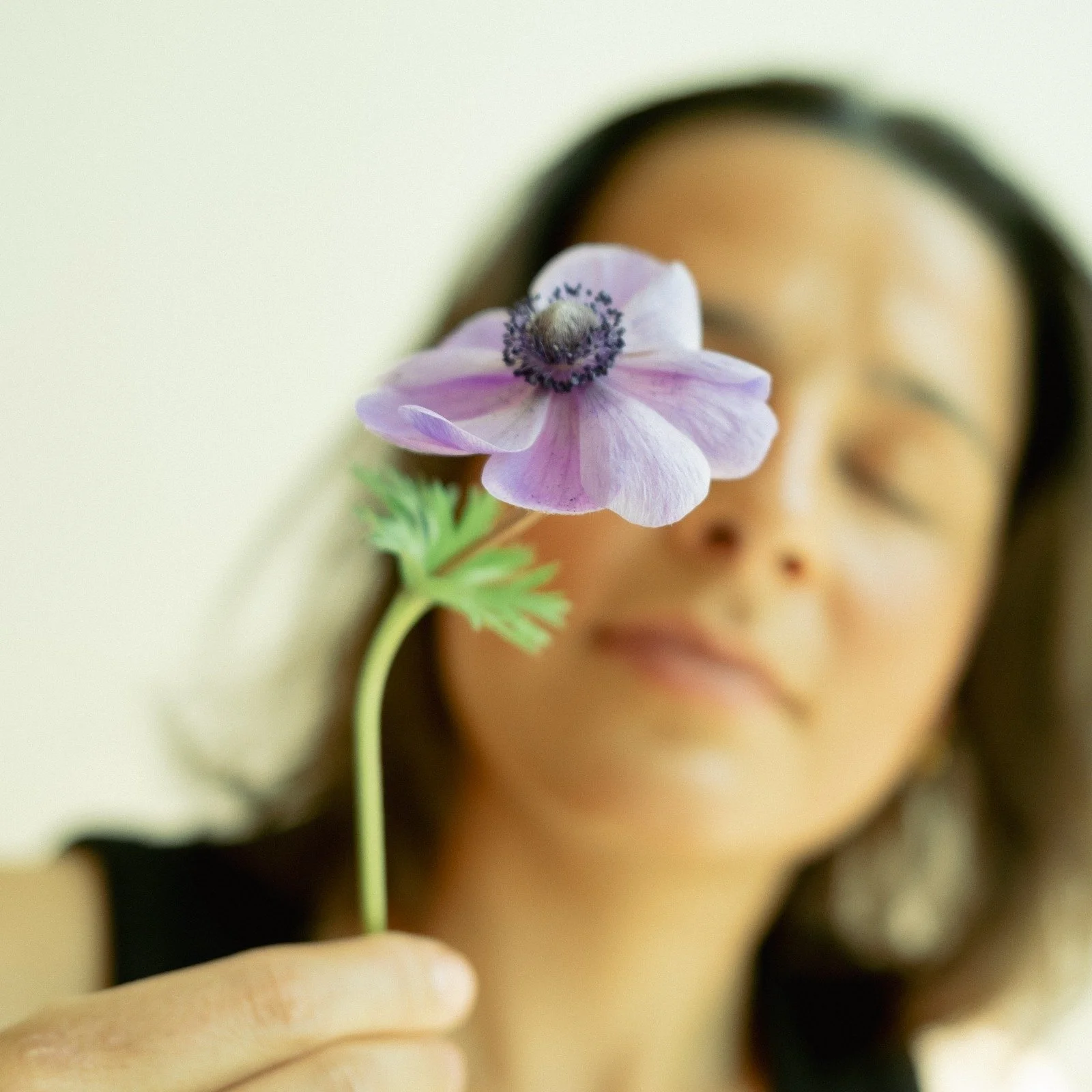 Frau hält eine lilafarbene Blume vor ihr Gesicht, while ihre Augen geschlossen sind.
