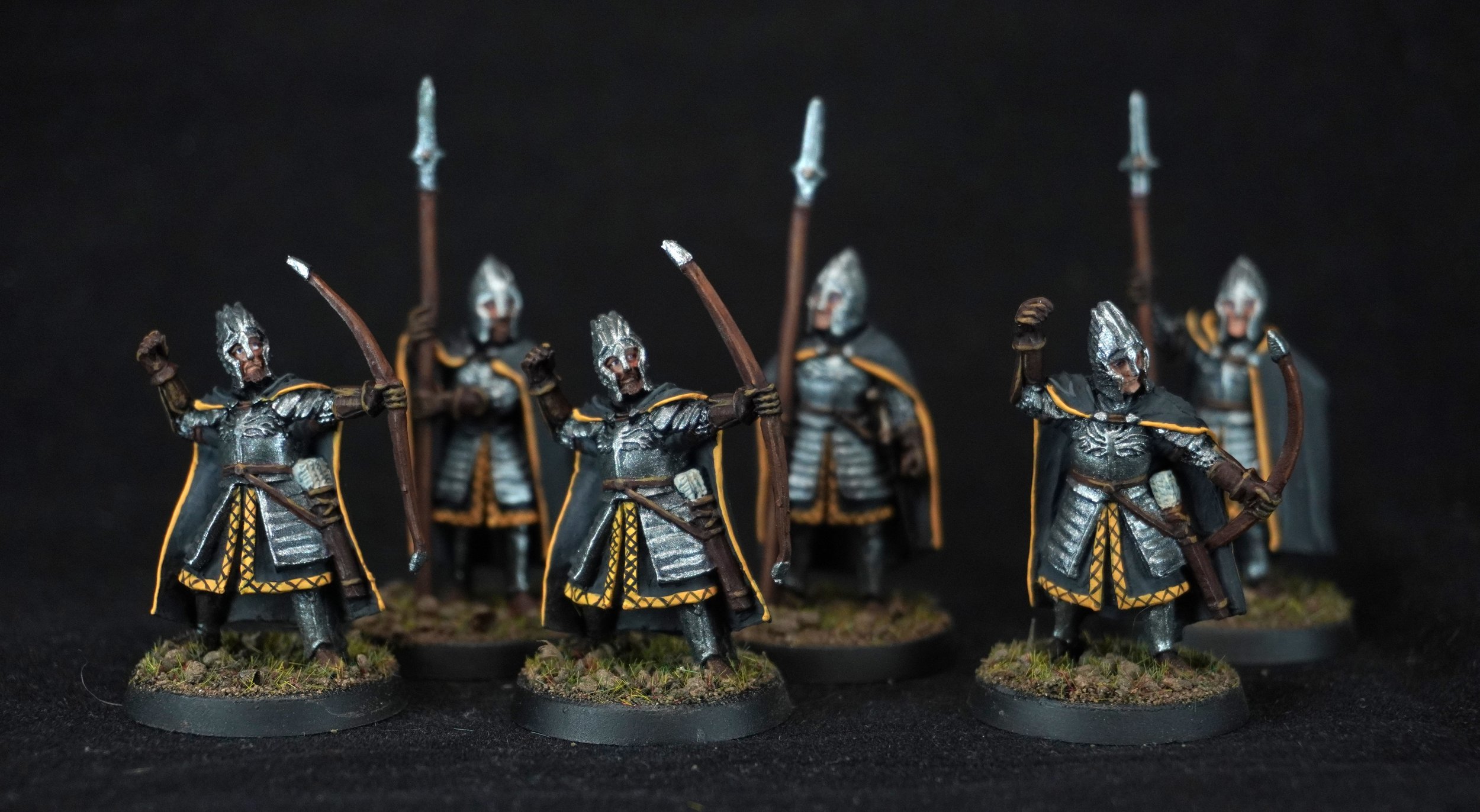 Miniature fantasy army soldiers wearing silver armor and black cloaks with yellow accents, wielding bows and arrows, standing on textured bases.