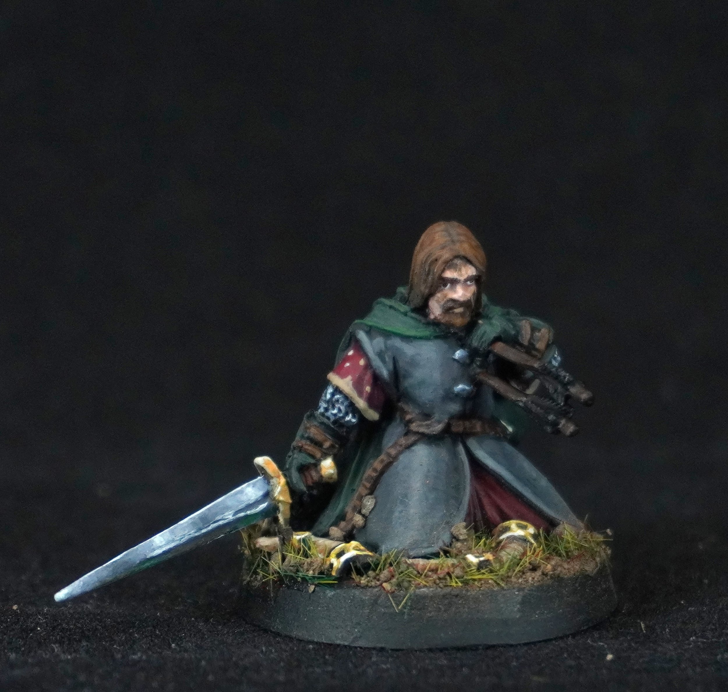 Miniature figurine of a medieval warrior with a sword and a crossbow, kneeling on a textured base with grass and small rocks, against a black background.