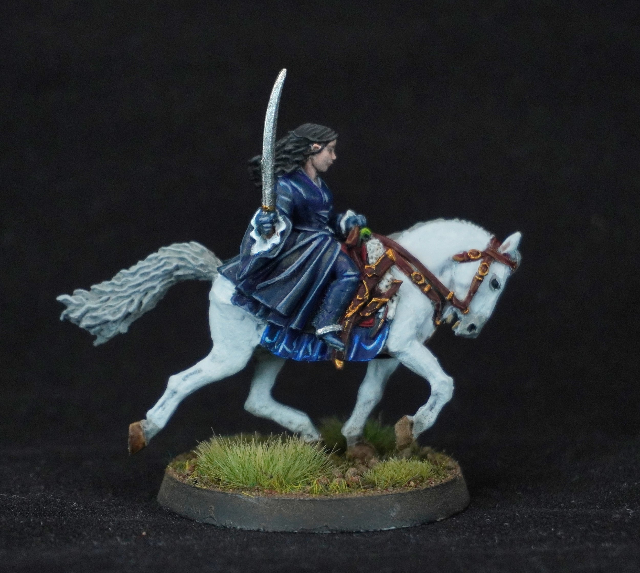 Miniature figurine of a woman riding a white horse, holding a sword, dressed in a blue outfit, on a grassy base.