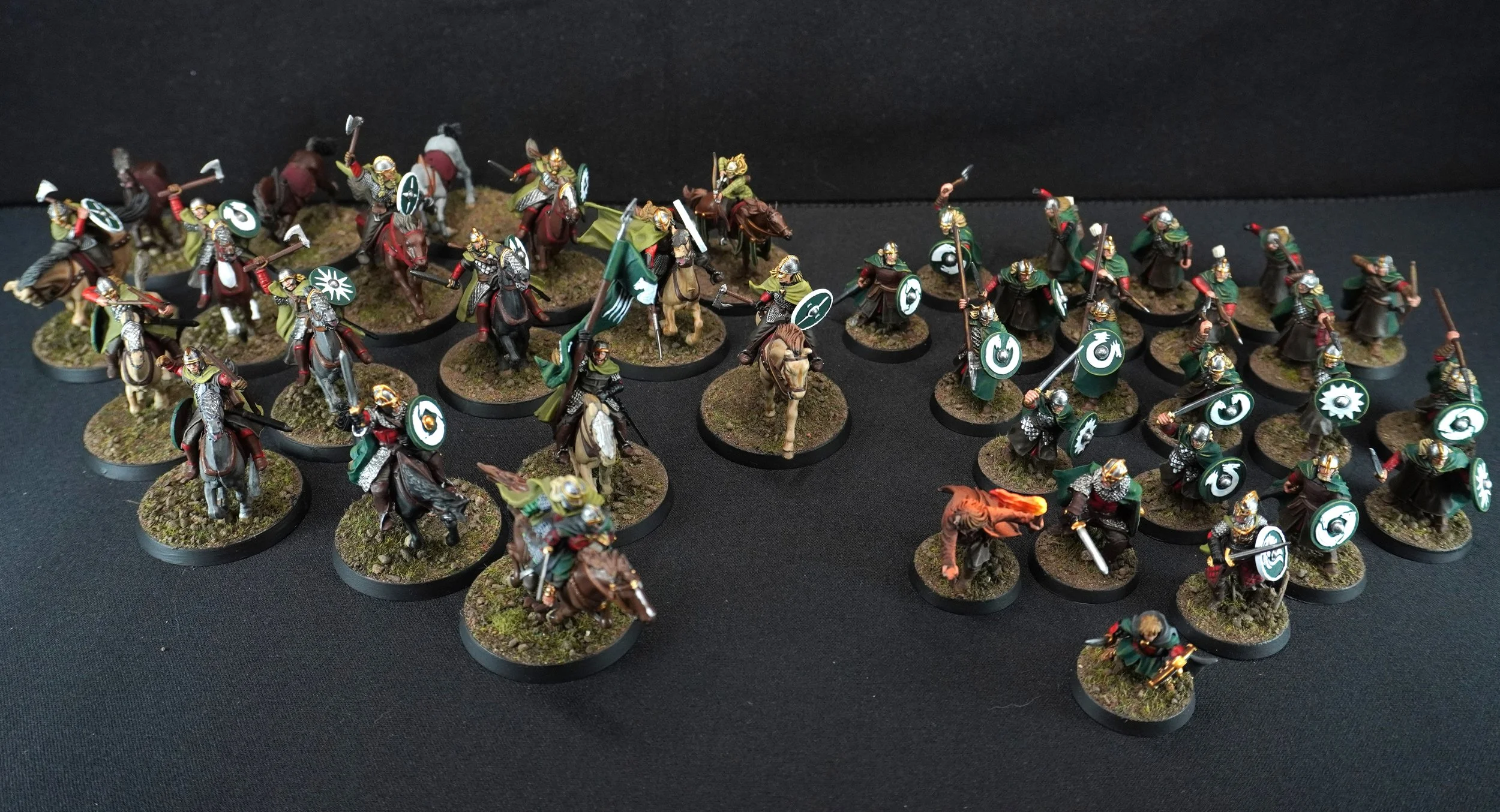 Miniature figurines of armored soldiers on horseback and on foot, carrying shields and weapons, arranged in formation on a black surface.