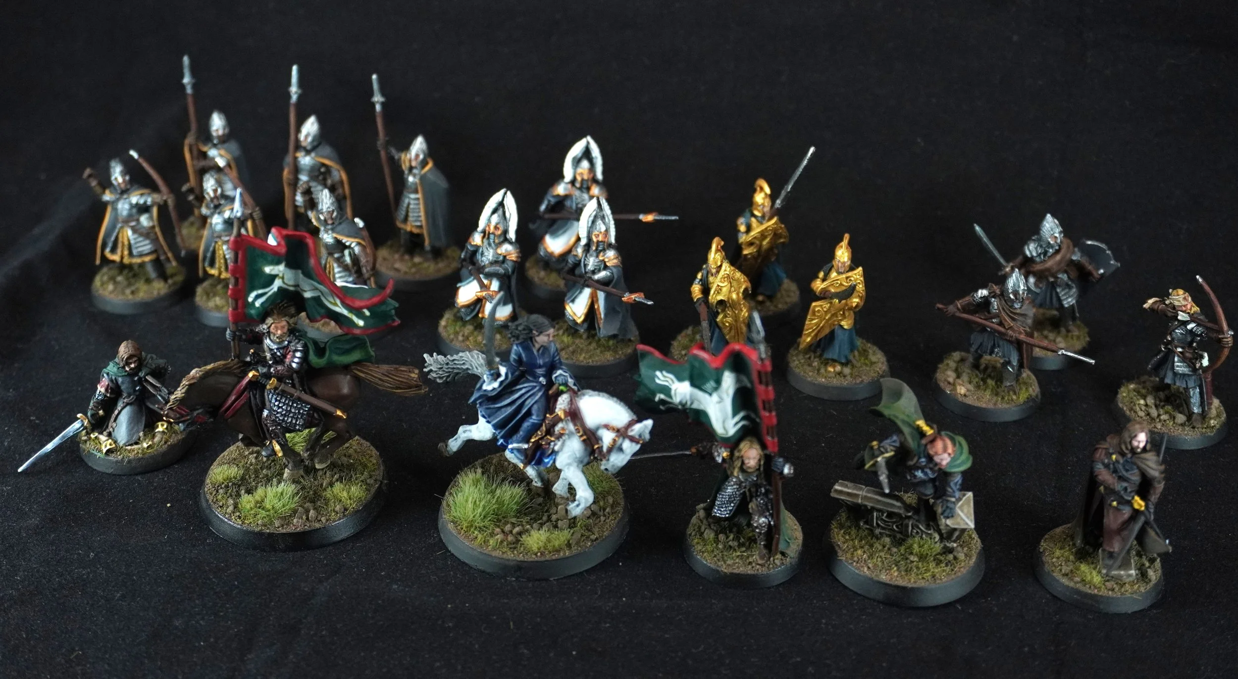 Collection of painted medieval fantasy miniature figurines on round bases depicting soldiers, knights, and warriors in armor, some holding flags, swords, or bows, arranged on a black surface.