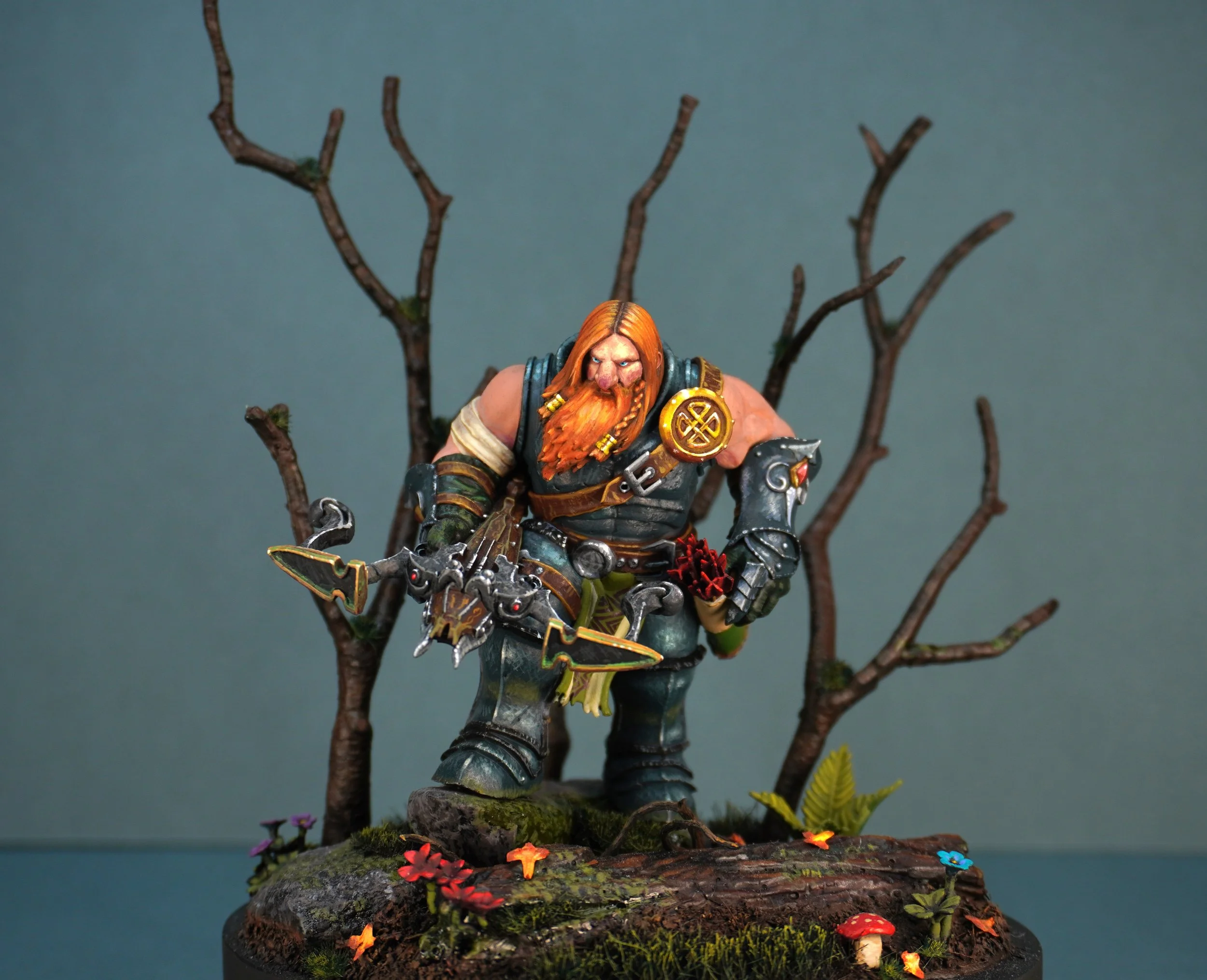 A detailed miniature figurine of a dwarf warrior with long red hair and beard, dressed in armor, holding a large weapon, standing on a base with moss, colorful mushrooms, and small flowers, with a backdrop of leafless trees.