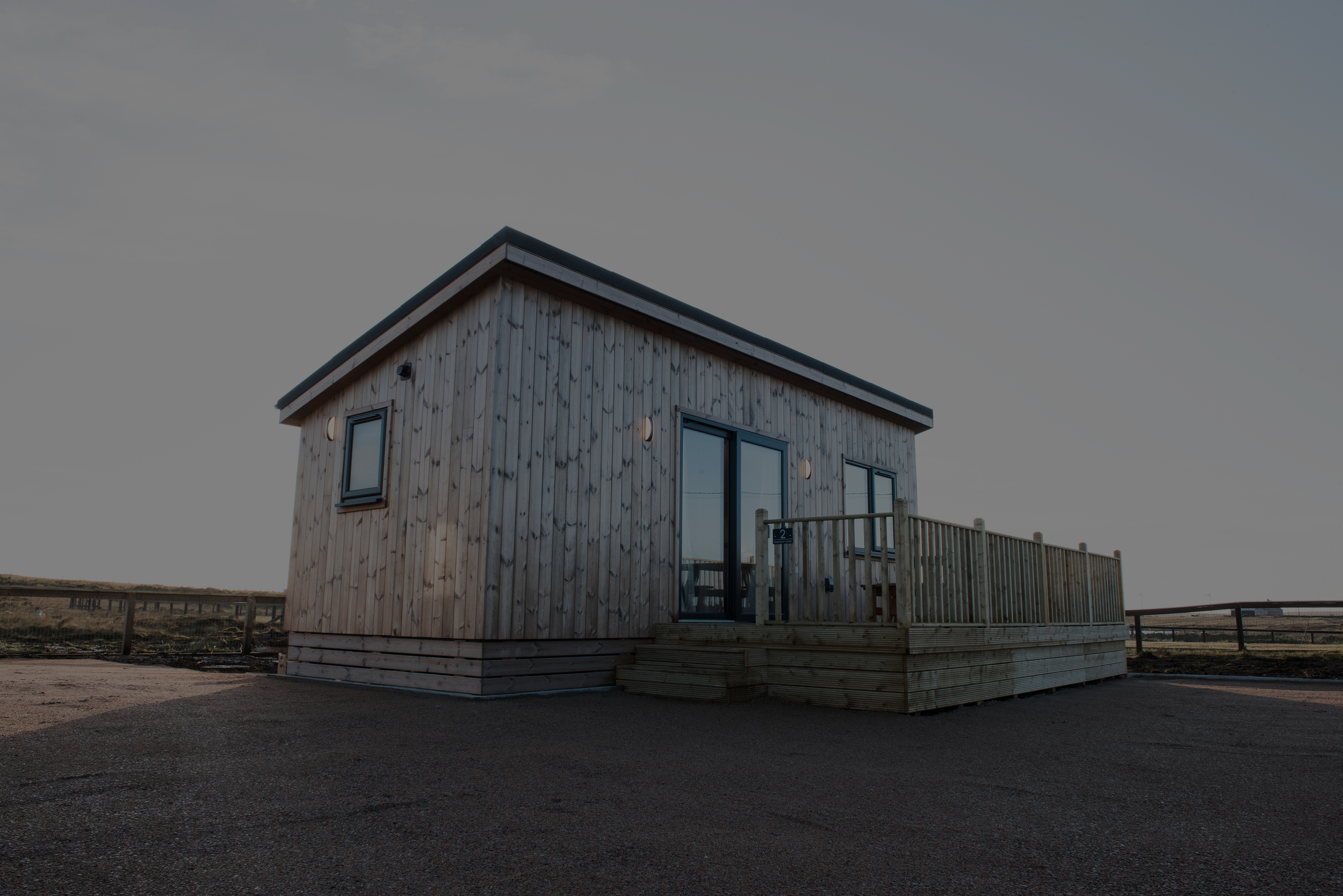 A small, modern wooden house with a ramp leading to its entrance, situated in an open landscape under a clear sky.