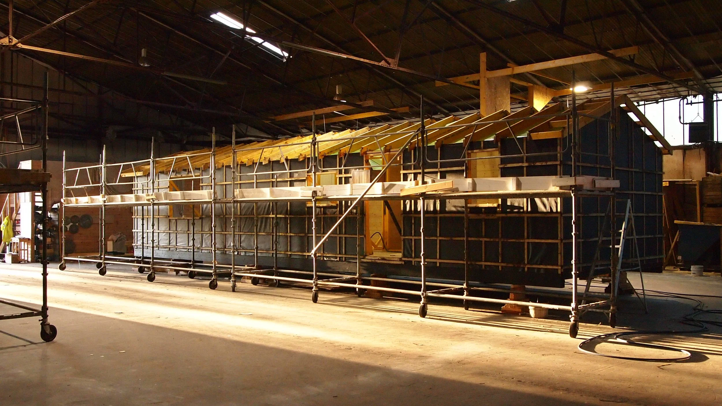 Construction site inside a large warehouse with partially built structure and scaffolding.