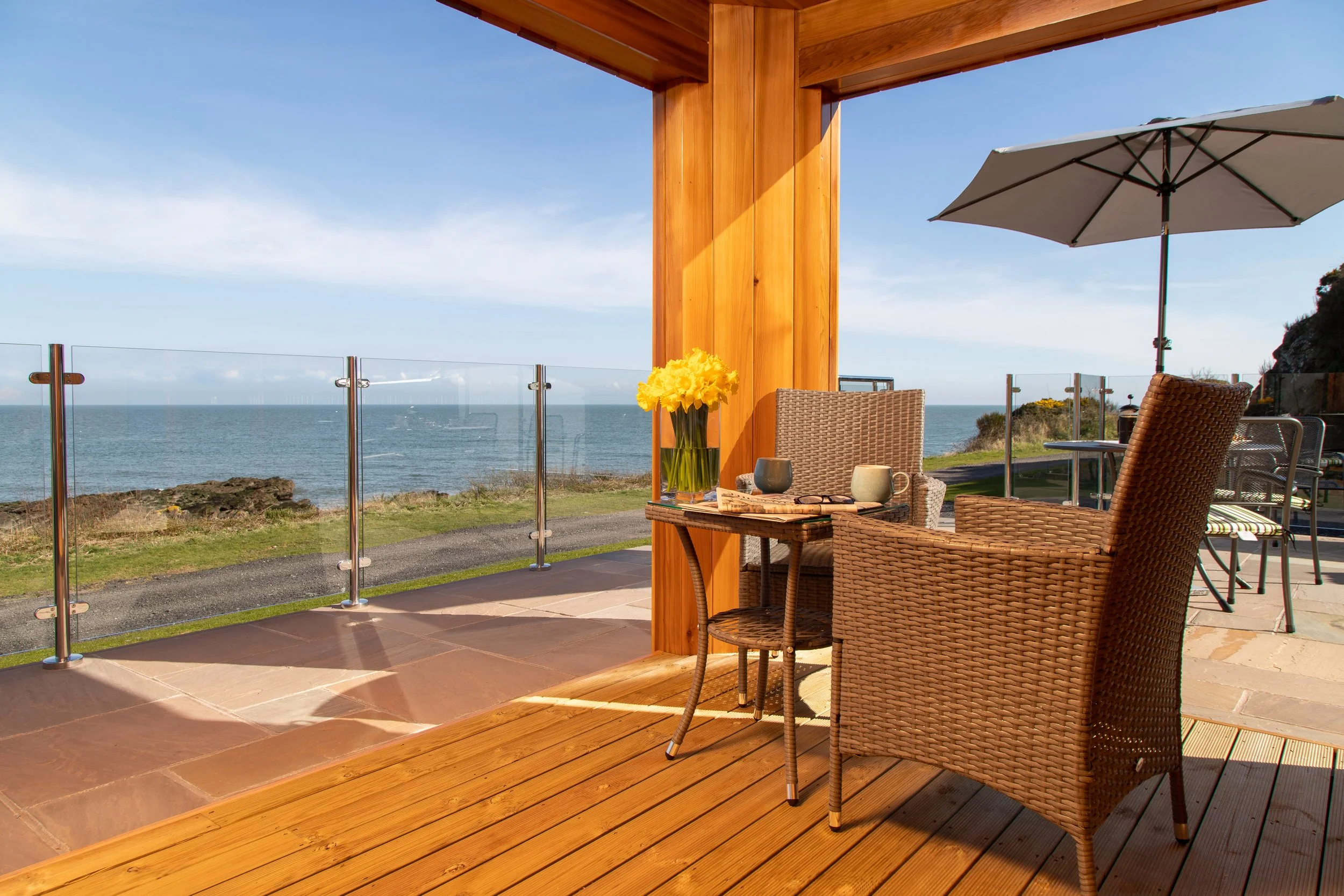 Outdoor patio with wicker chairs, a glass railing, umbrella, and ocean view in the background.
