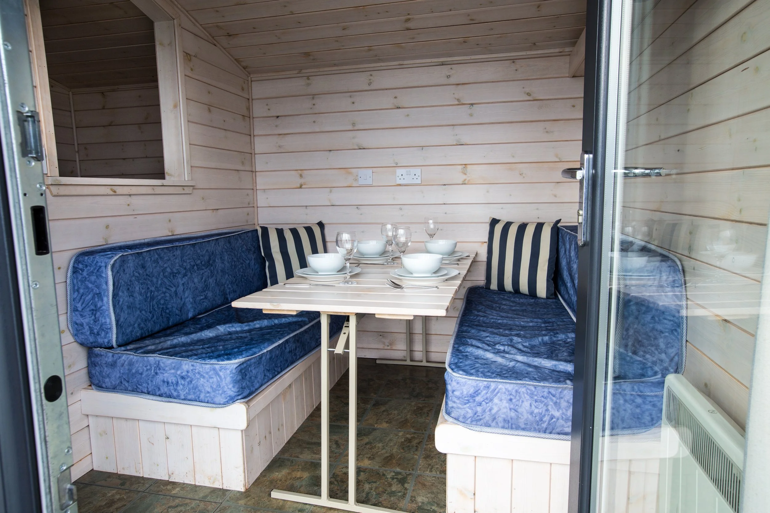 Indoor dining area with built-in wooden benches, a small table set with bowls, glasses, and cutlery, inside a wooden-paneled room