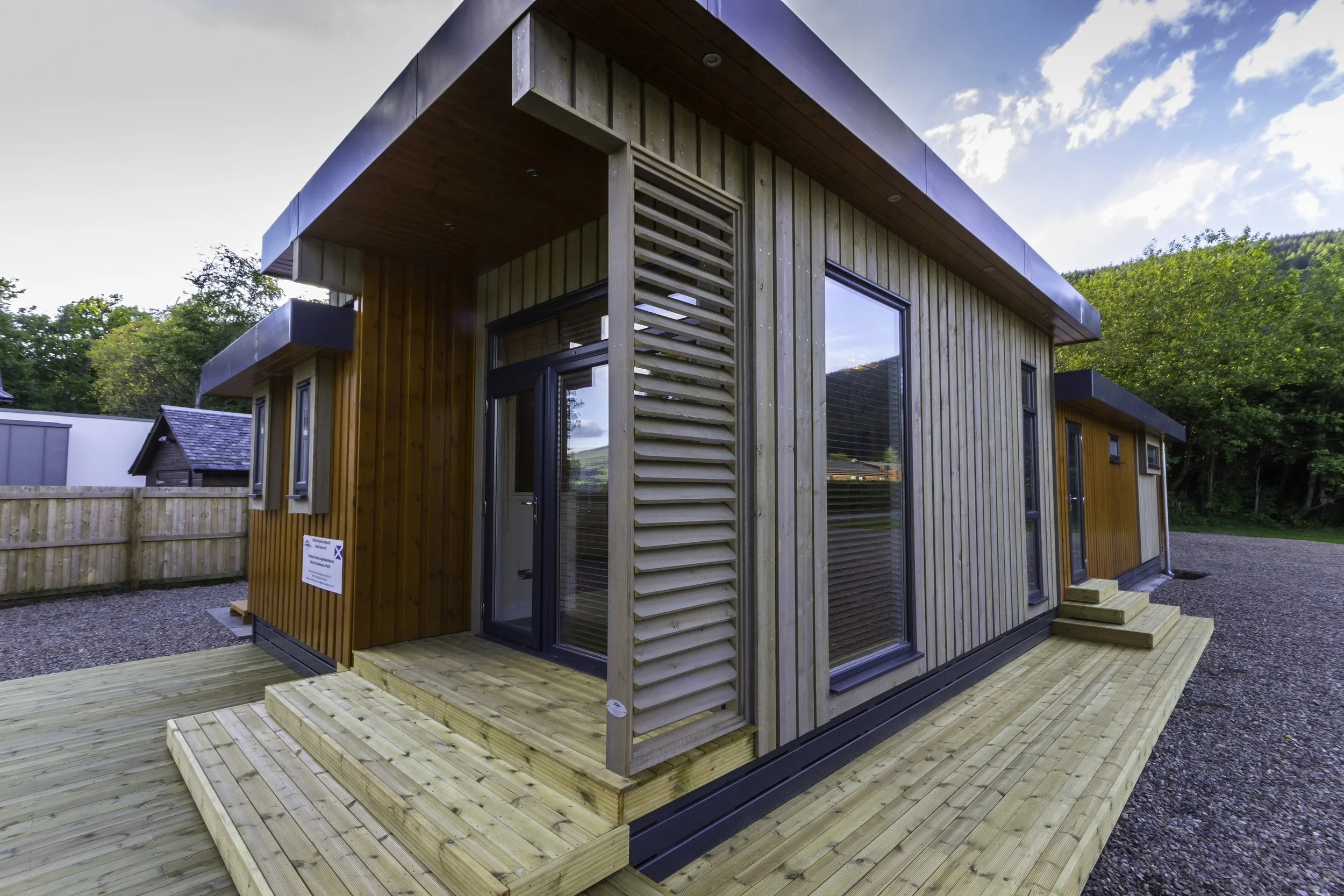 Modern wooden building with large glass windows, a small deck with steps, and outdoor landscaping.
