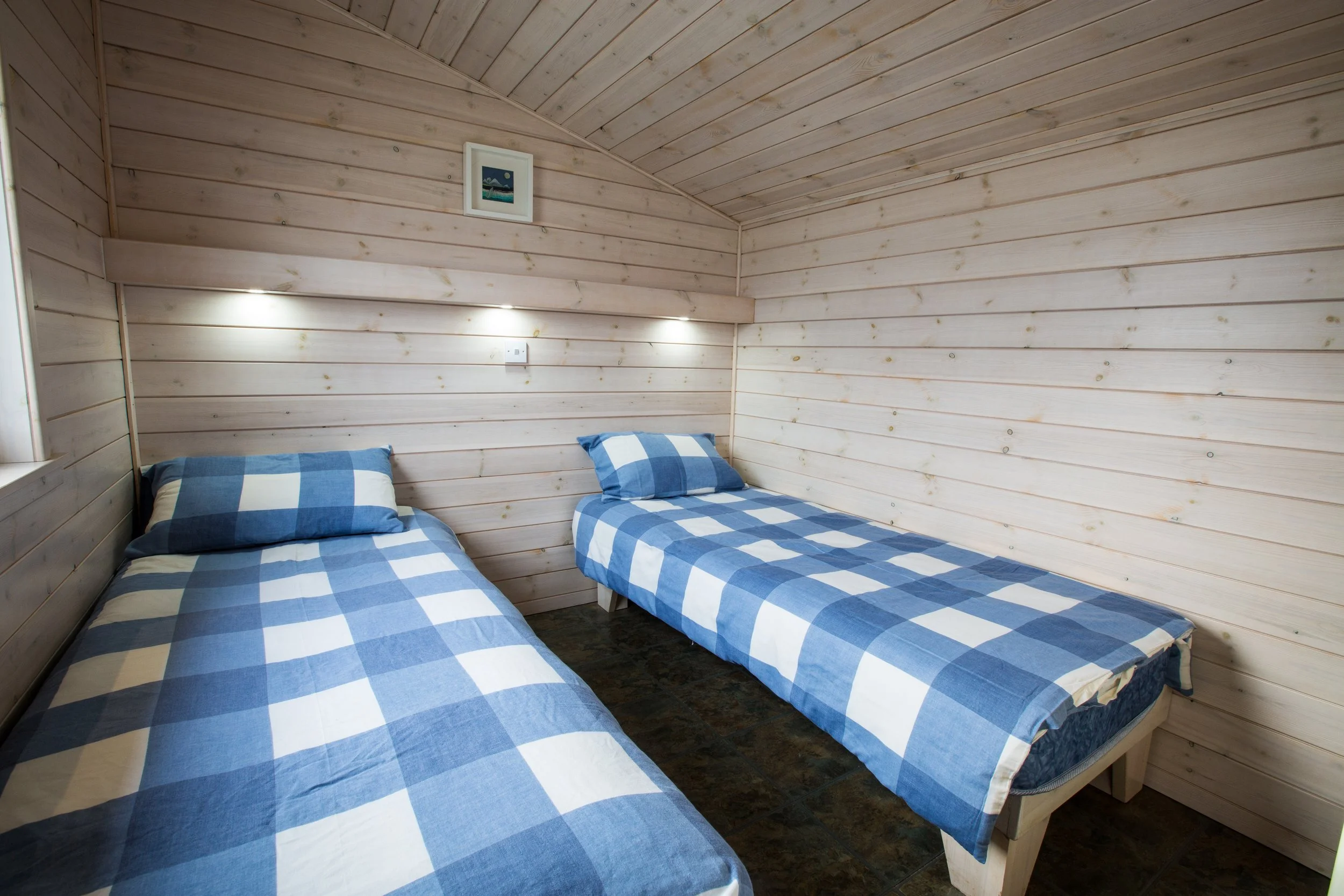 Two single beds with blue and white checkered bedding in a wooden-paneled room.