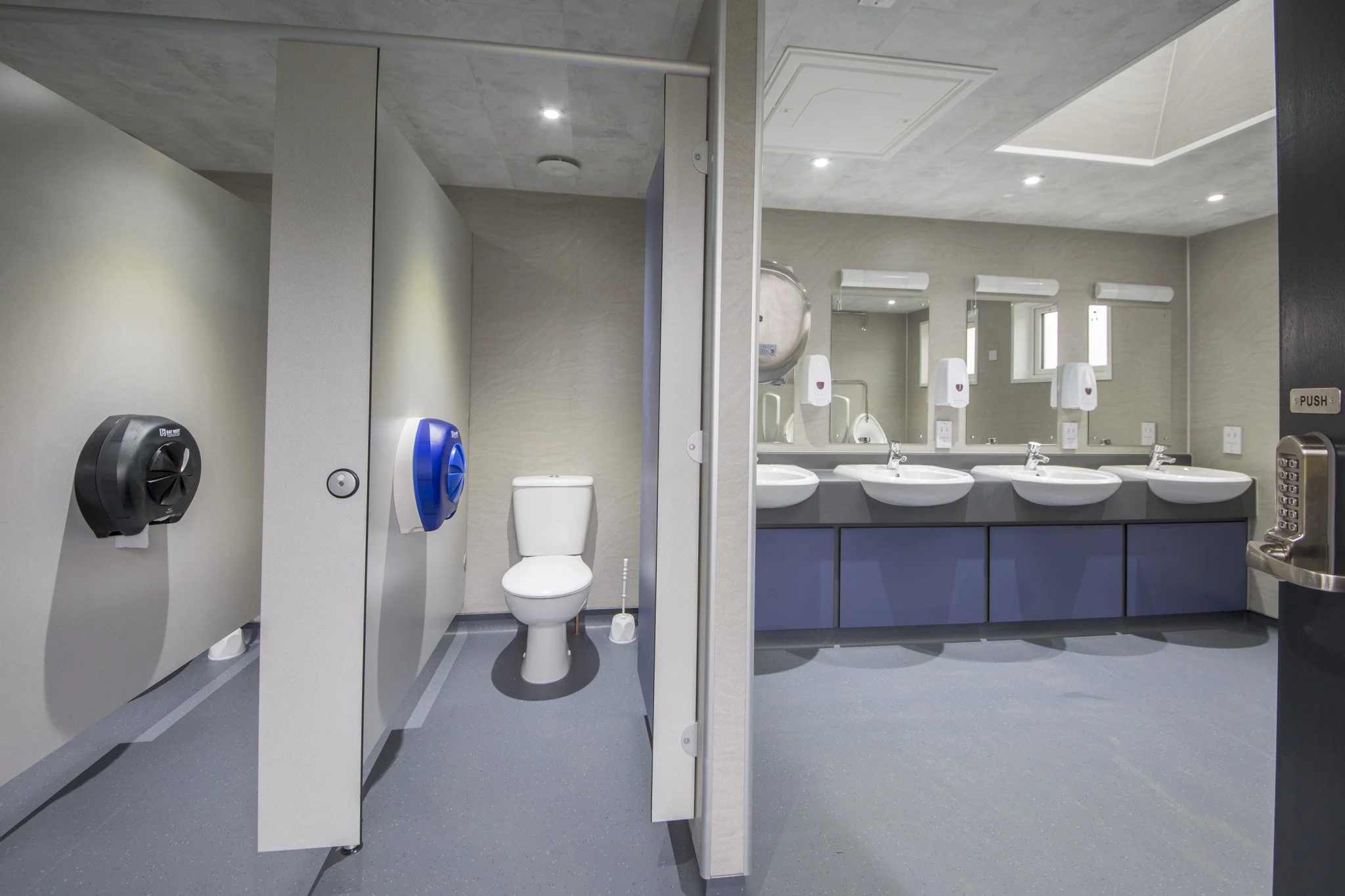 Public restroom with a toilet, hand sanitizer dispensers, and a three-sink vanity with mirrors.