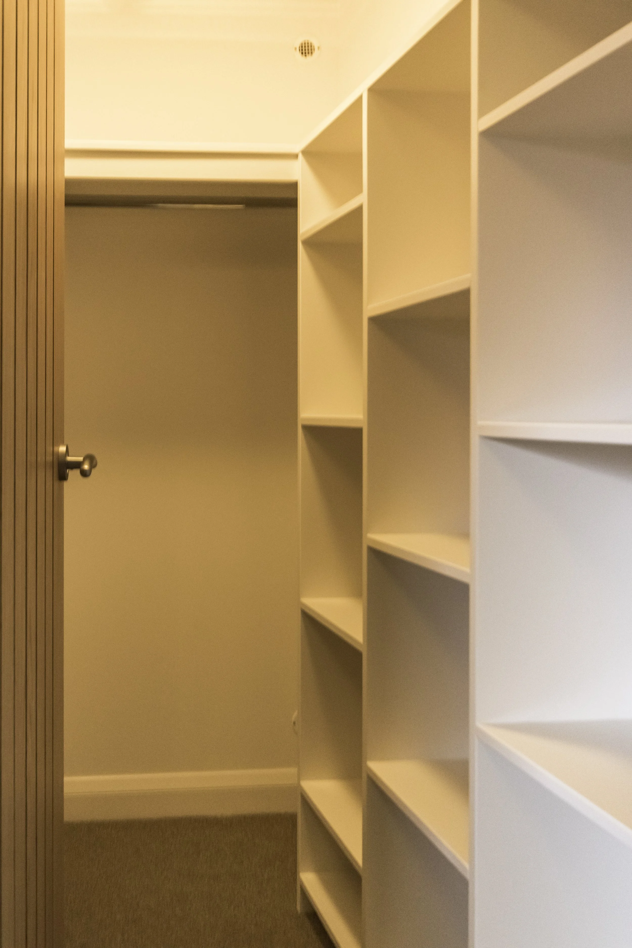 Empty walk-in closet with white shelving units and beige walls.