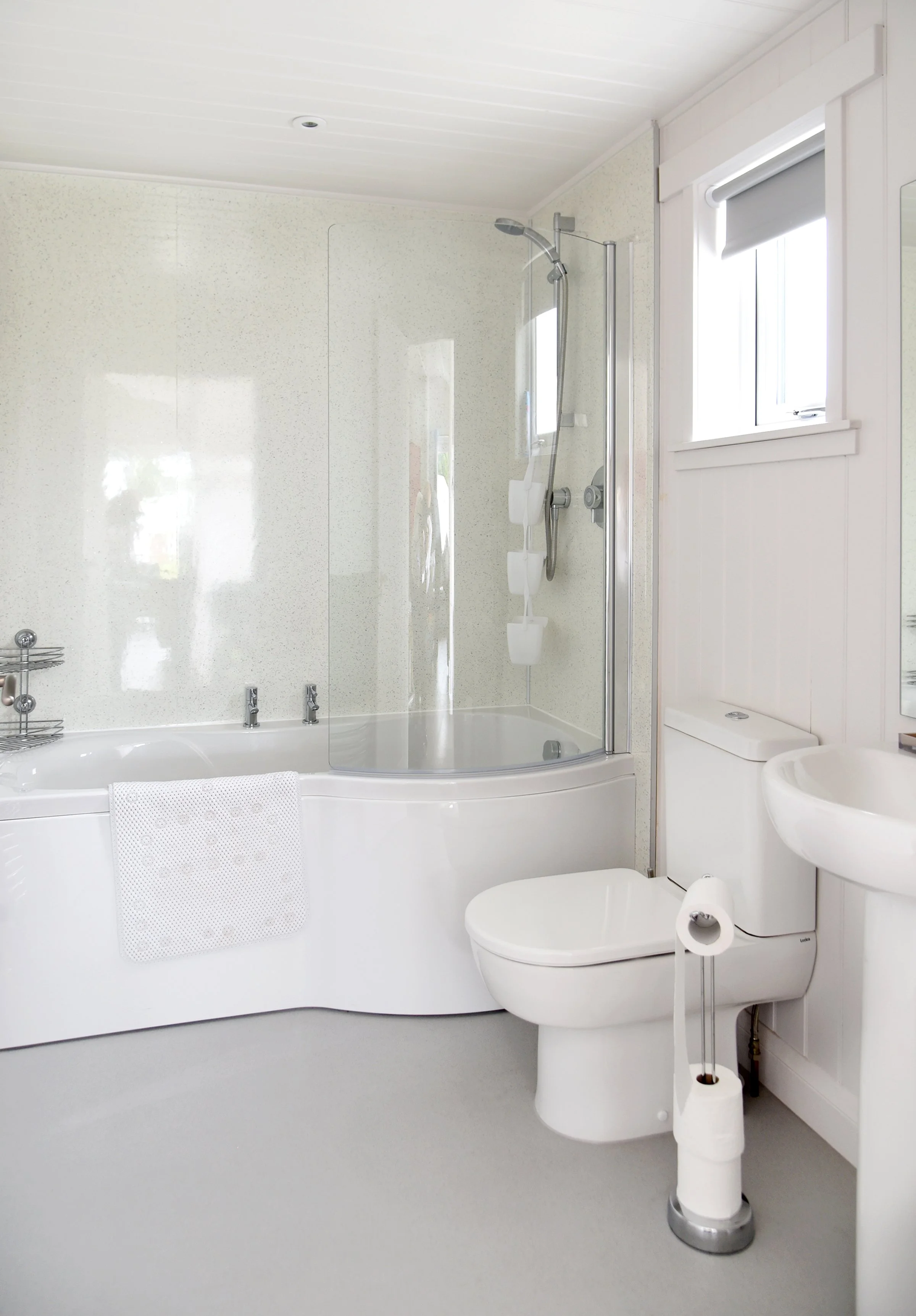 Modern white bathroom with a bathtub, shower, toilet, small sink, and window.