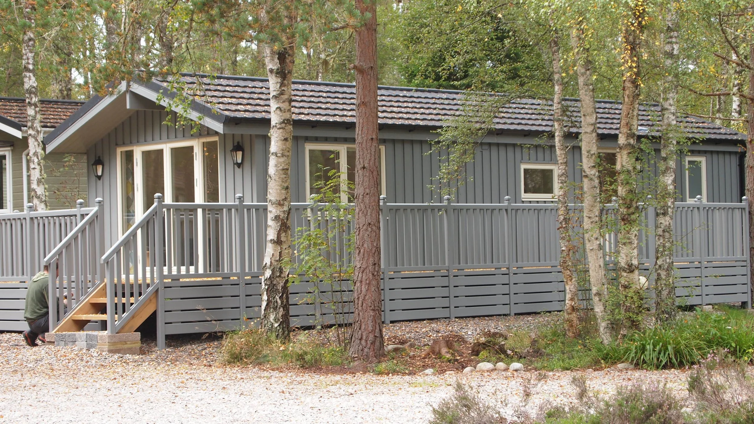 A gray house with a raised deck surrounded by trees and shrubbery