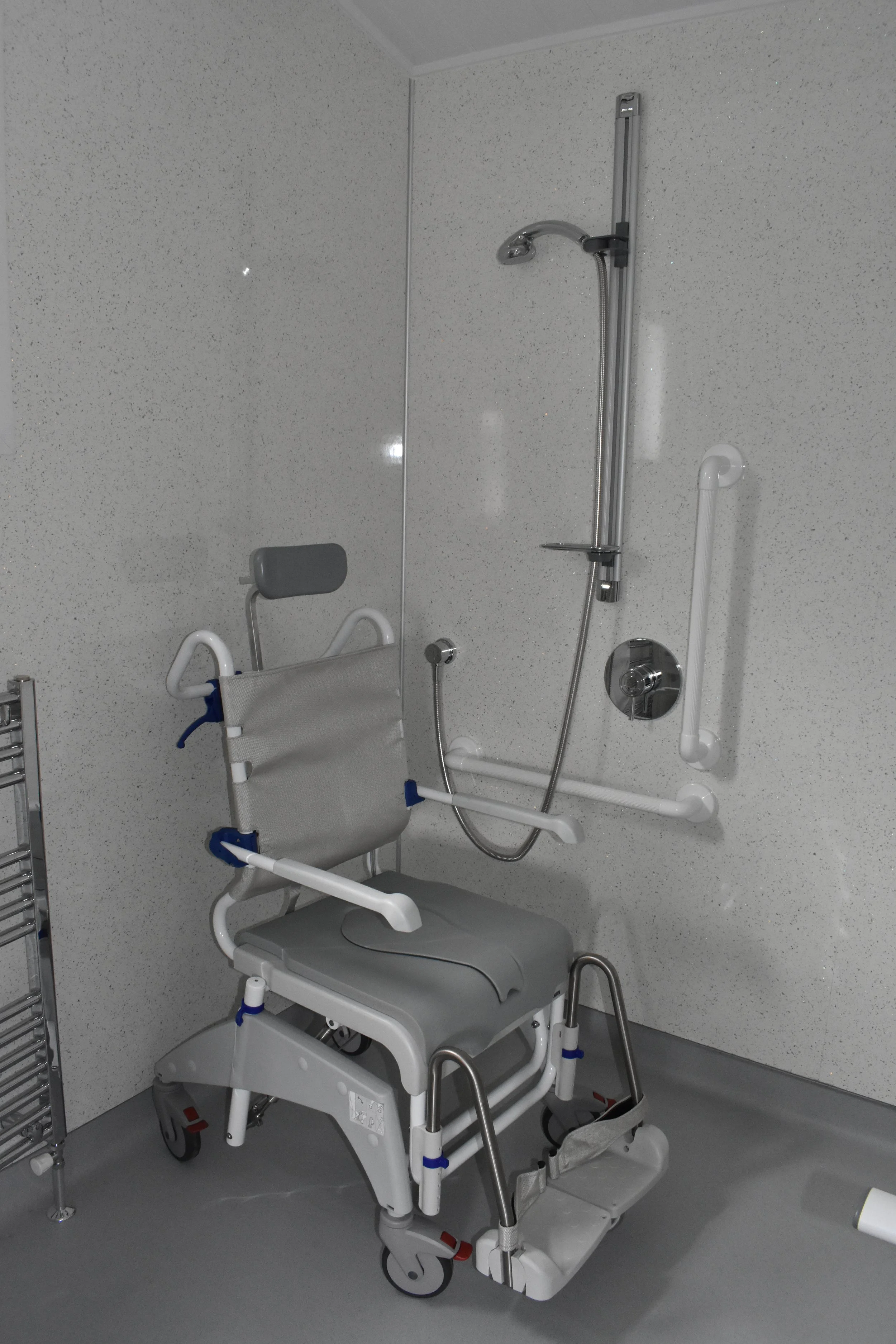 Hospital shower with wheelchair accessible fixtures, grab bars, and a shower chair.
