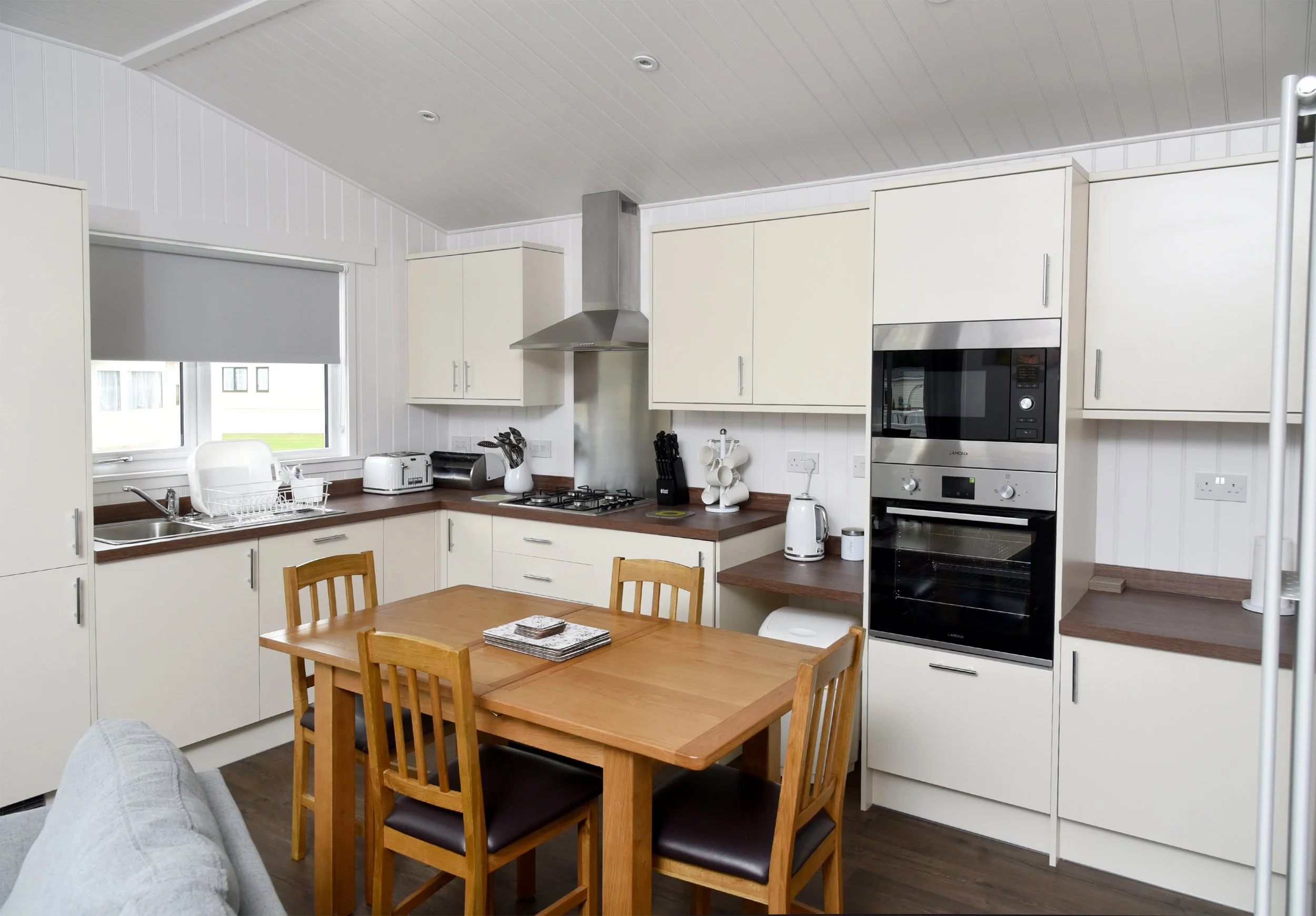 Kitchen with white cabinets, wooden table and chairs, stainless steel appliances, and a window with a blind