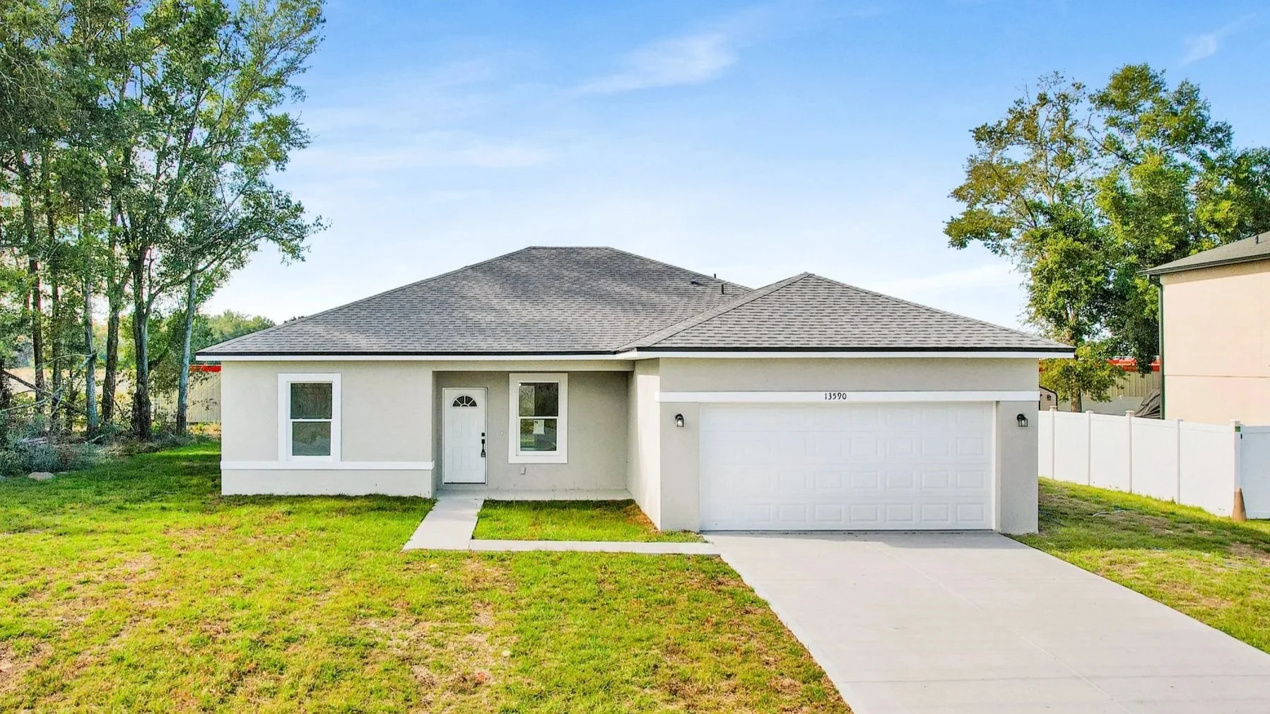 Backyard with patio furniture, green grass, white fence, and two-story beige house with sliding glass door and windows under a blue sky.